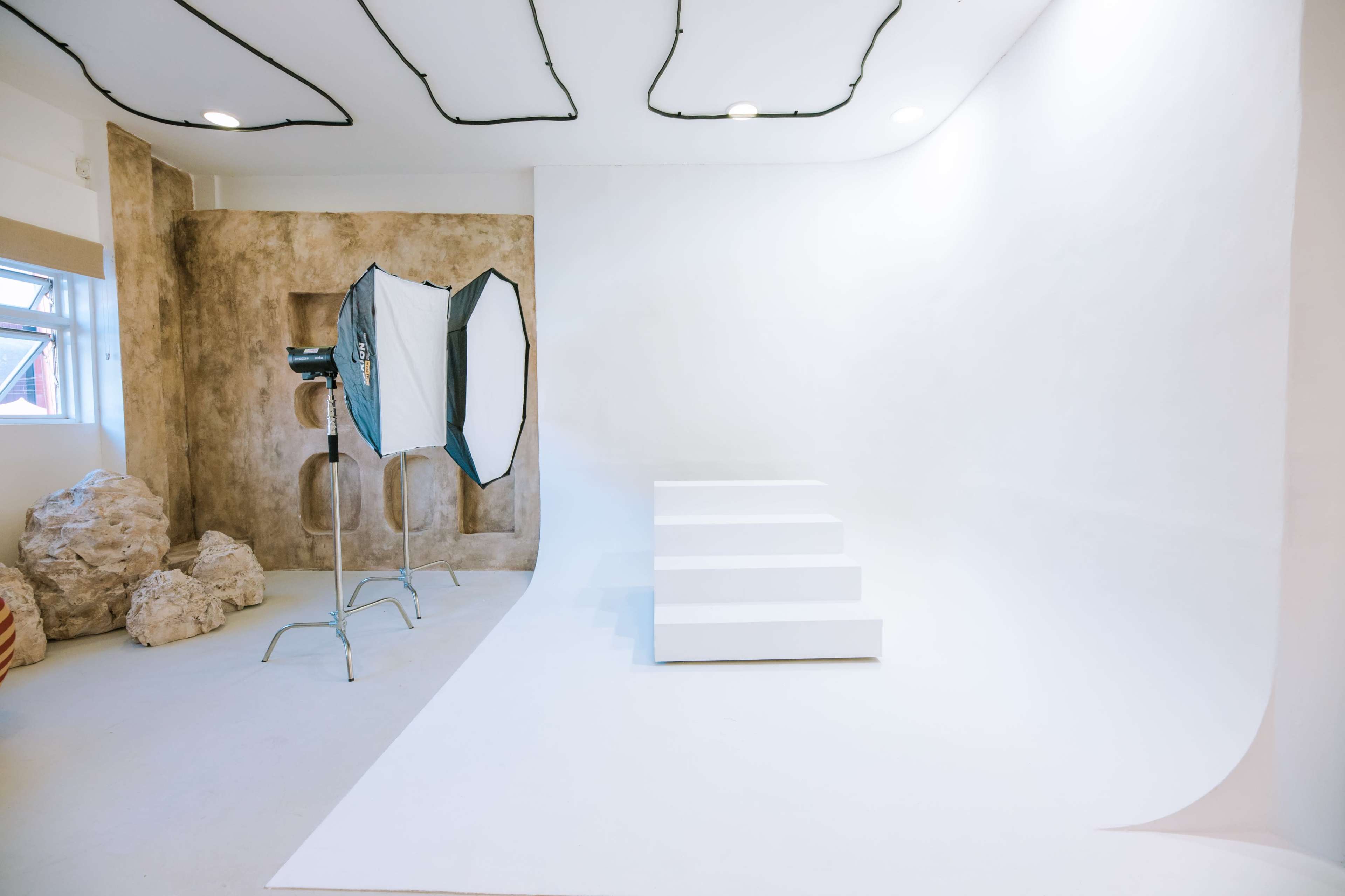 The image shows a photography studio featuring a white seamless backdrop, a set of white steps, and a light source with an umbrella modifier.