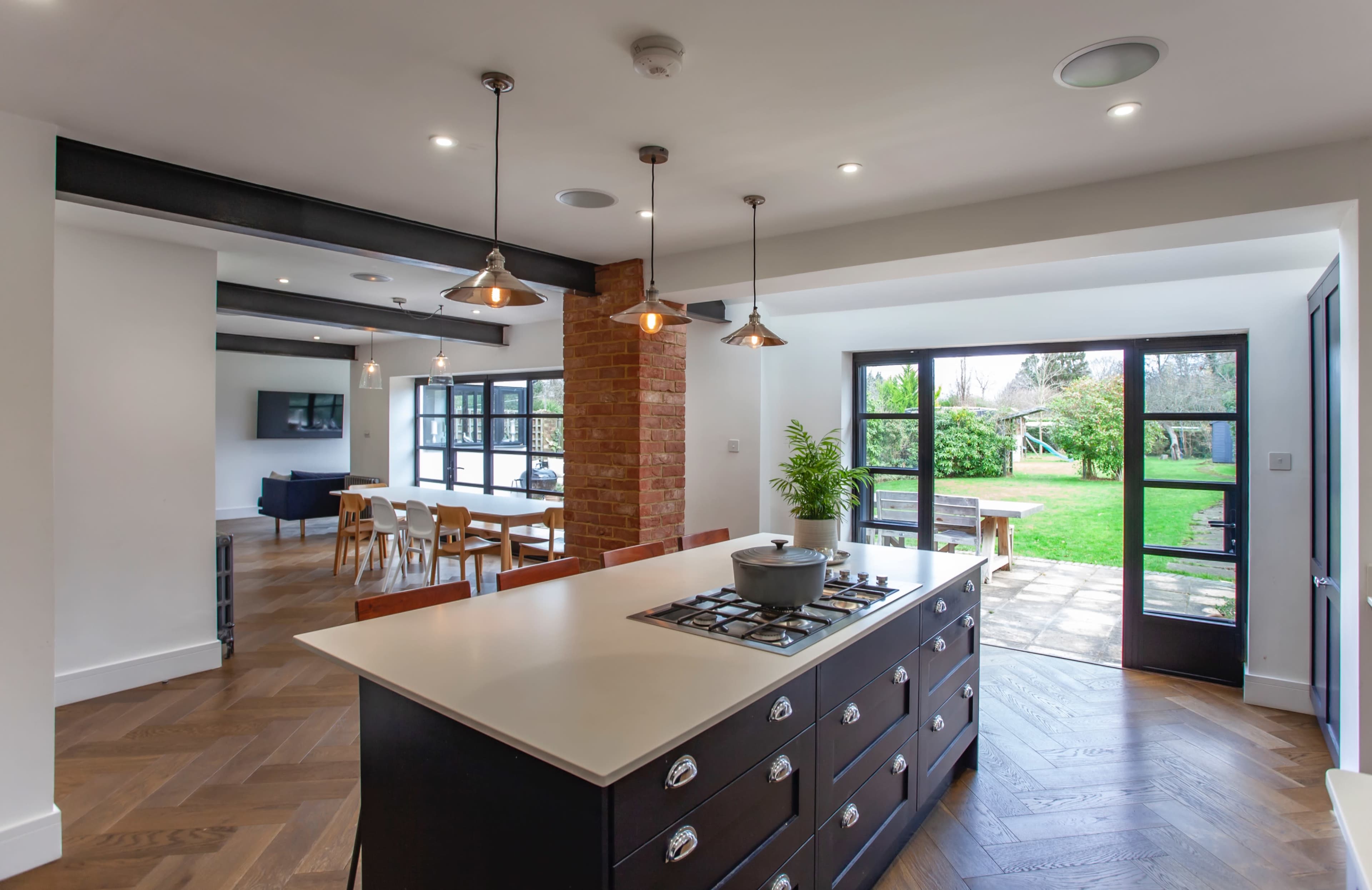 A modern kitchen with a large island and a view of an outdoor garden area, featuring a mix of wooden and brick elements.