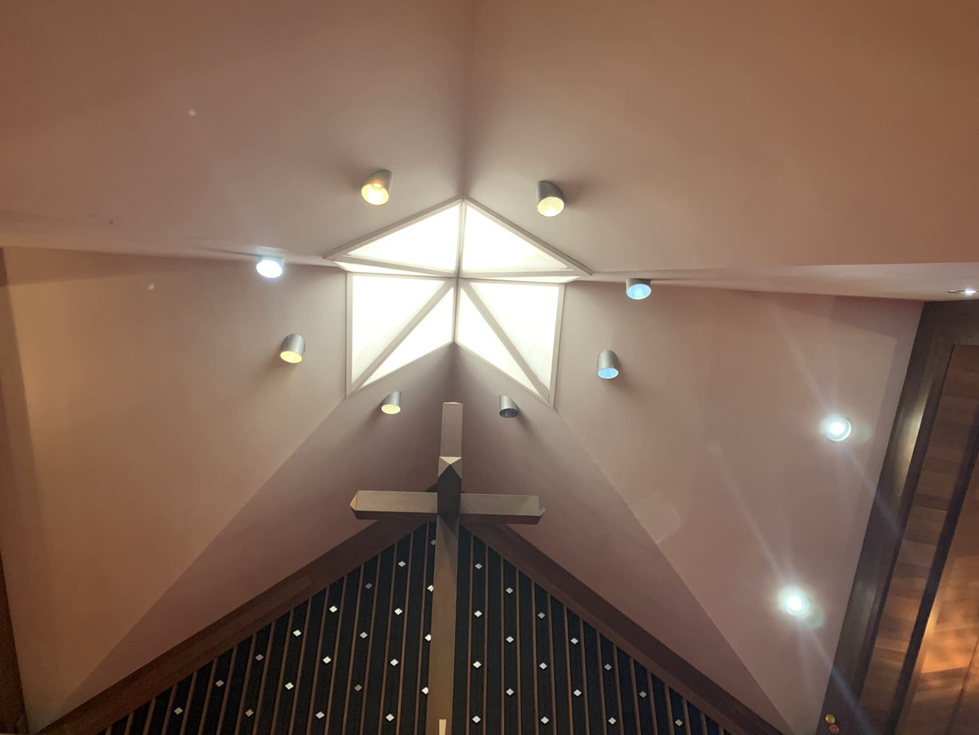 The interior ceiling of a church with a central cross and a star-shaped light feature illuminated by various colored bulbs.