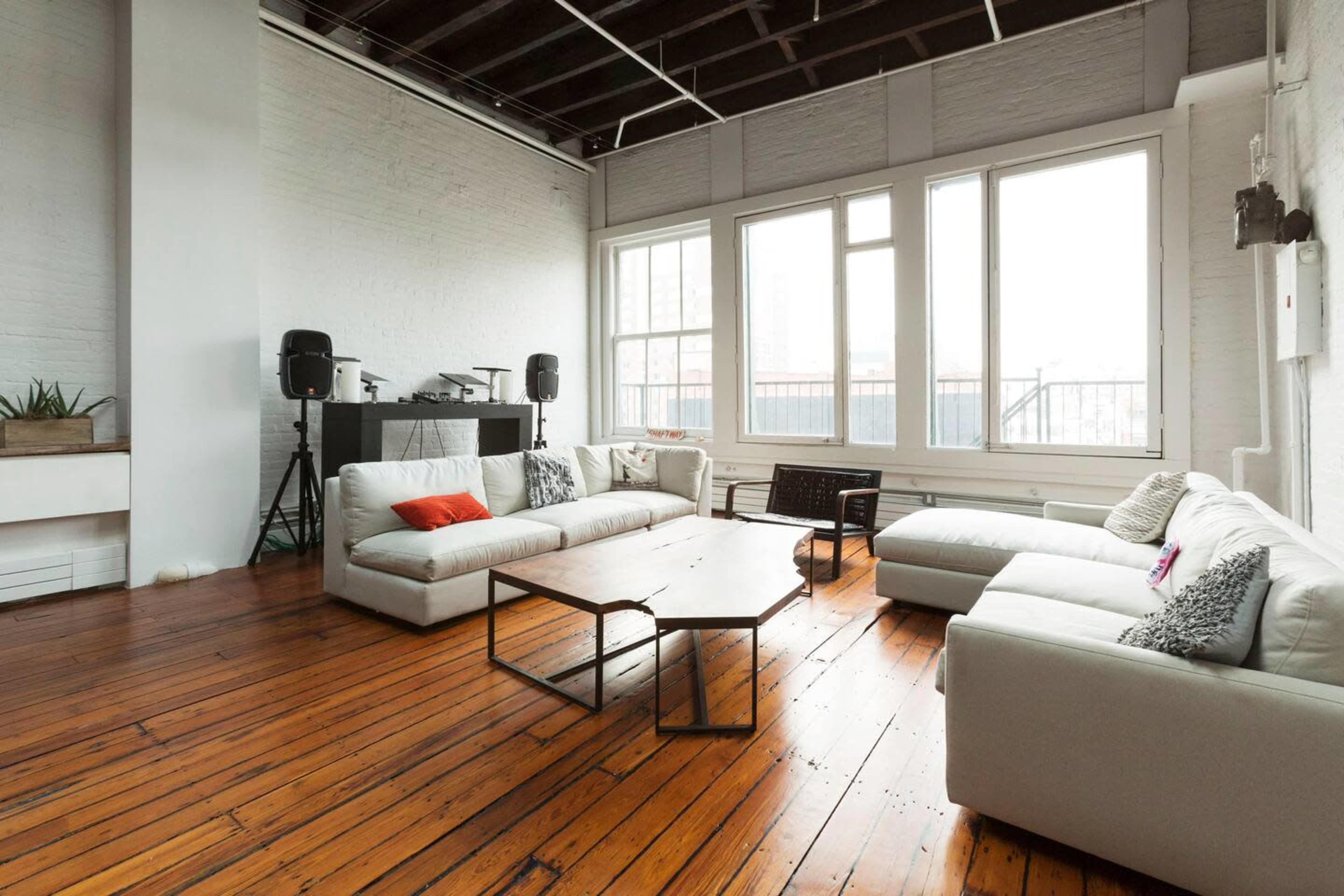 A spacious room with large windows, hardwood floors, and a seating arrangement consisting of a white sectional sofa and a coffee table.
