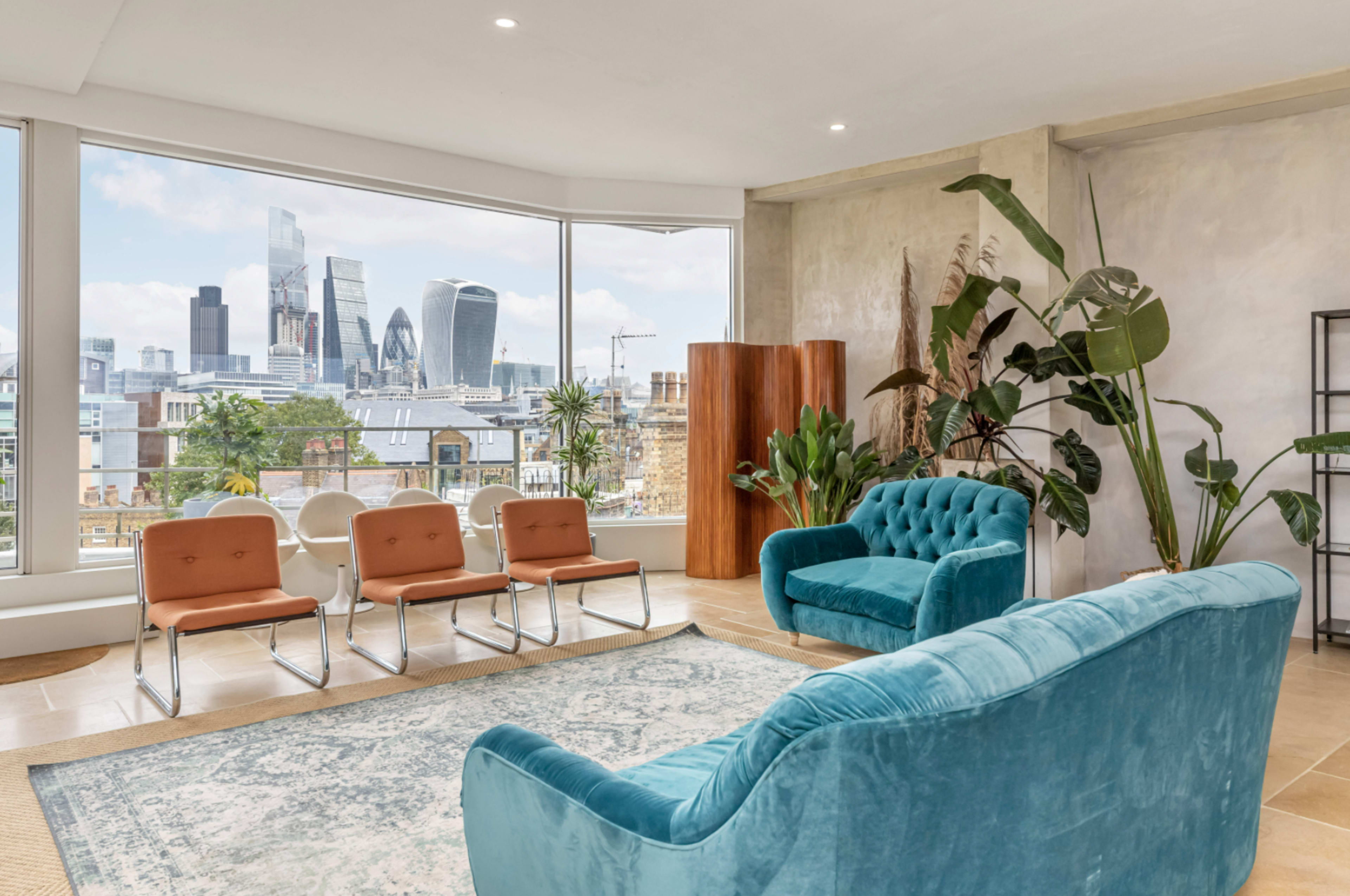 A modern living area features a turquoise sofa, metal chairs, and large windows revealing a city skyline.