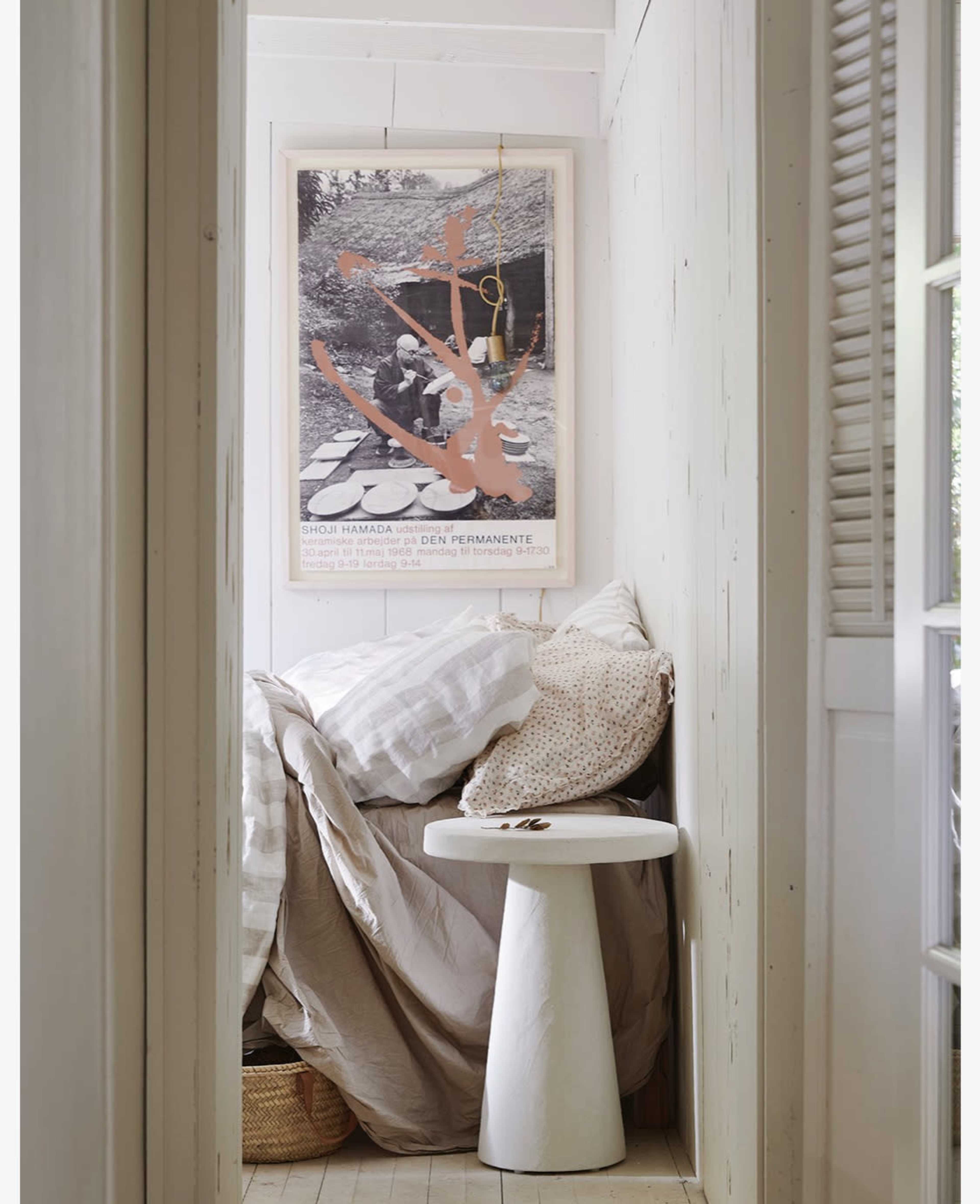 The scene features a narrow hallway with a modern white pedestal table, a textured blanket, and a large framed artwork on the wall.