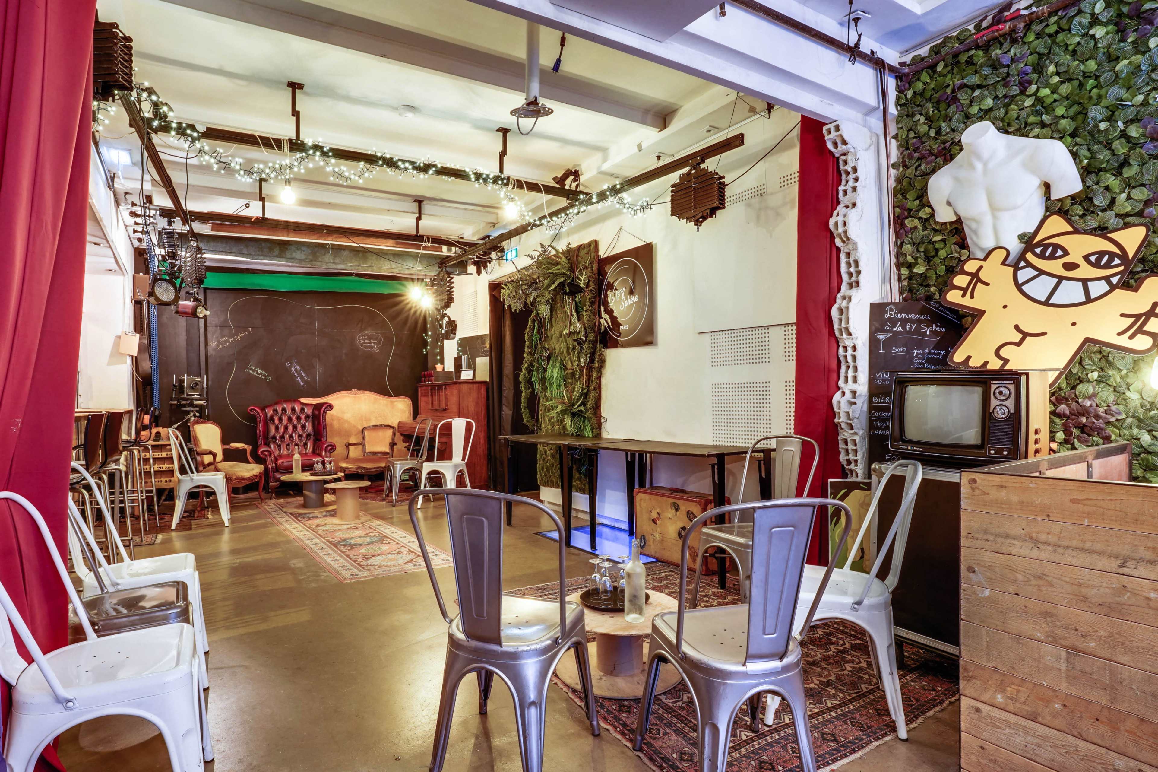 A cozy café interior with metal chairs, a vintage television, and decorative plants on the walls.