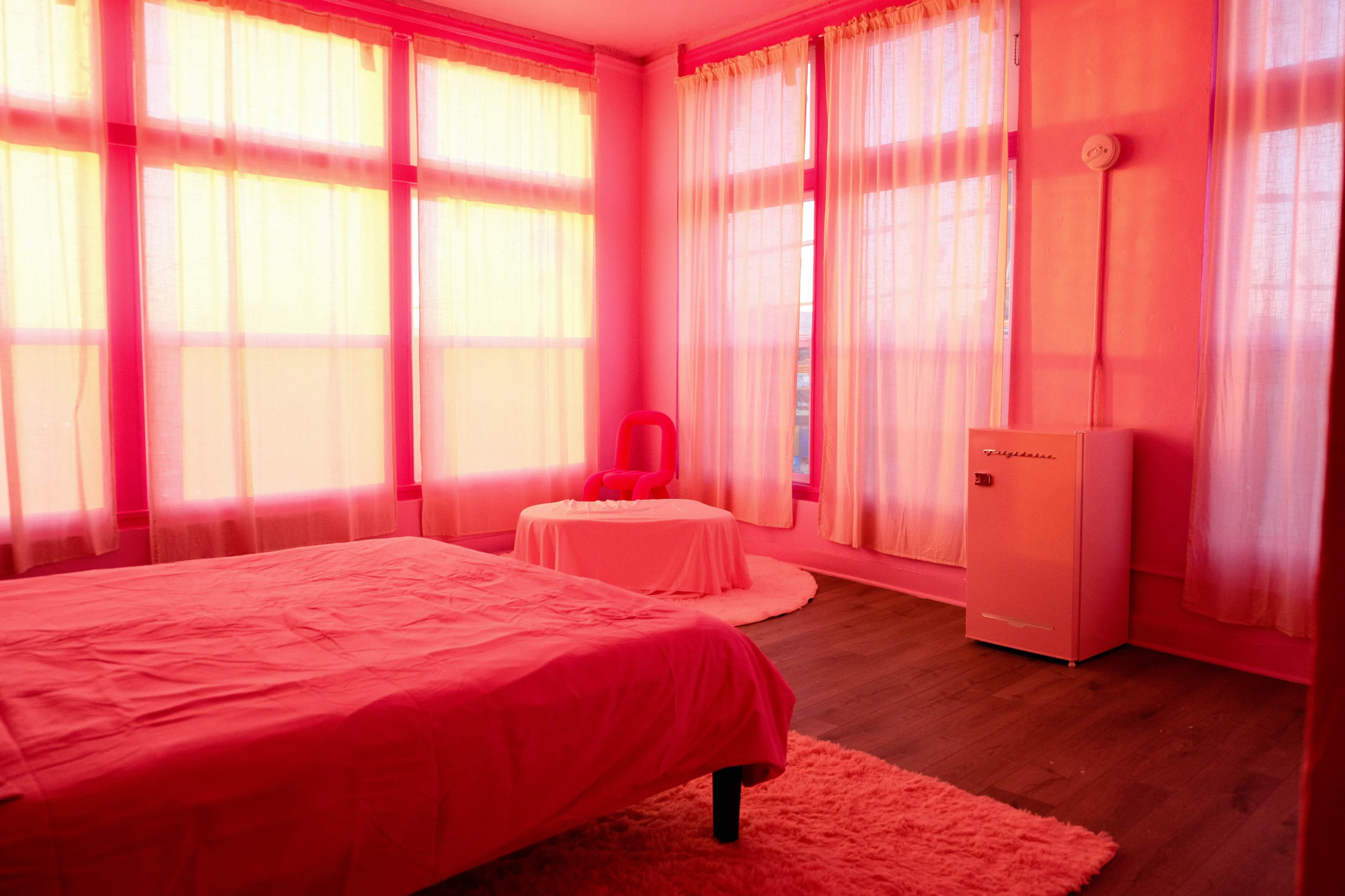 The room features pink walls, drapes, and bedding, with large windows allowing natural light to fill the space.