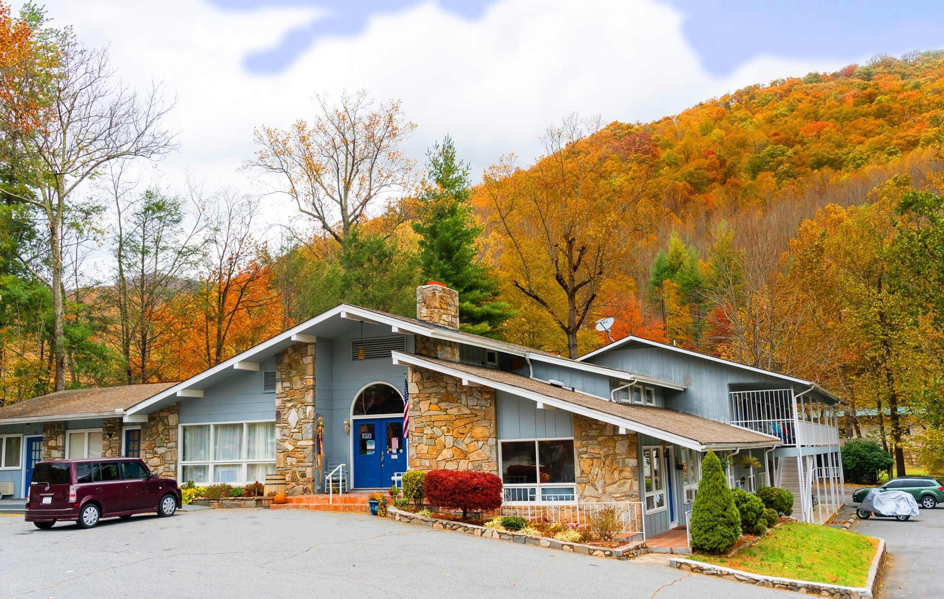 A modern building with stone accents is situated in front of a wooded hill displaying colorful autumn foliage.