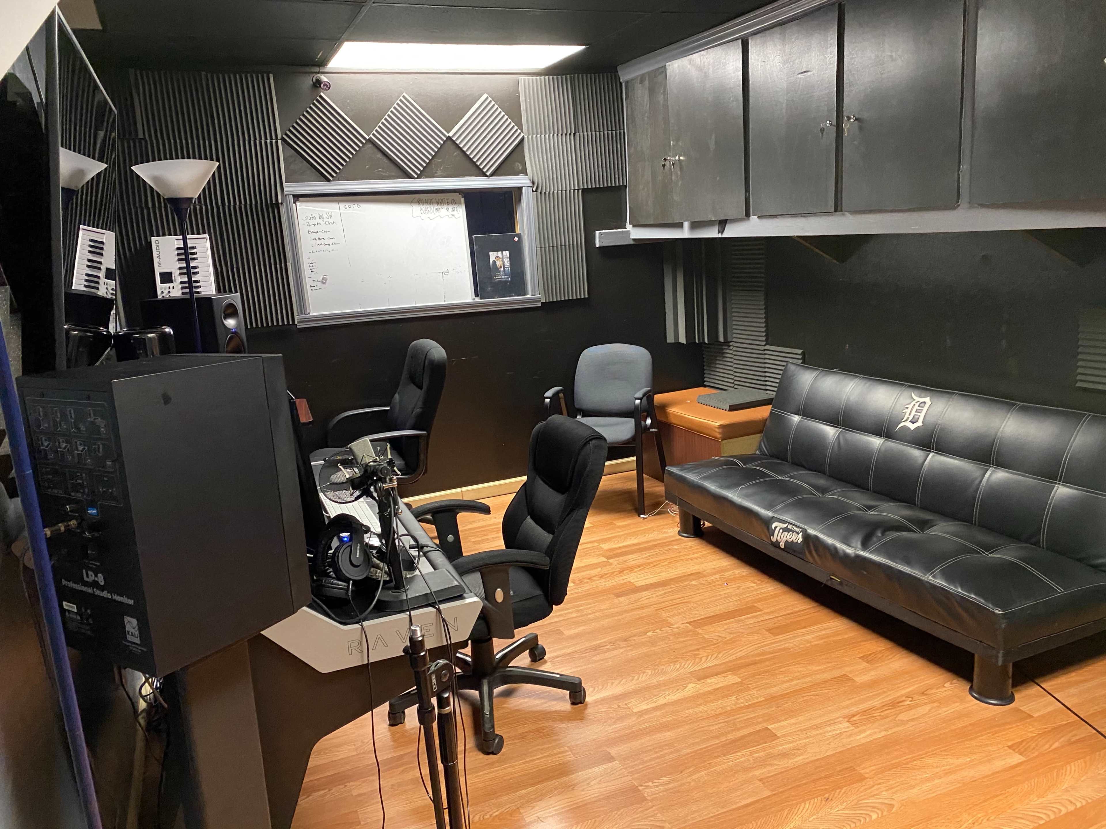A music studio featuring a black futon, several audio monitors, and a desk with computer equipment.