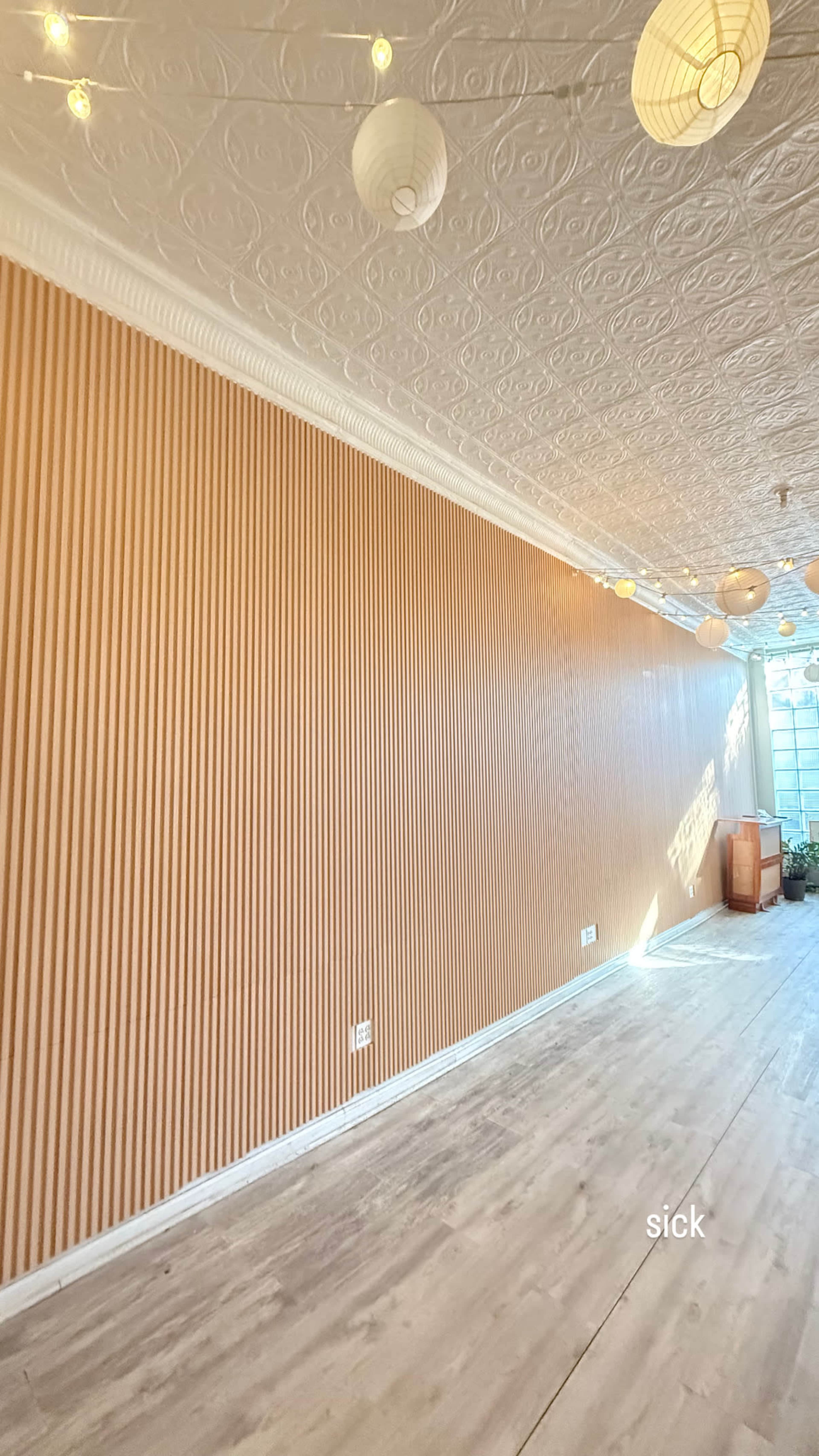 The image shows a well-lit interior space with a textured, ridged wall and decorative hanging lanterns above.