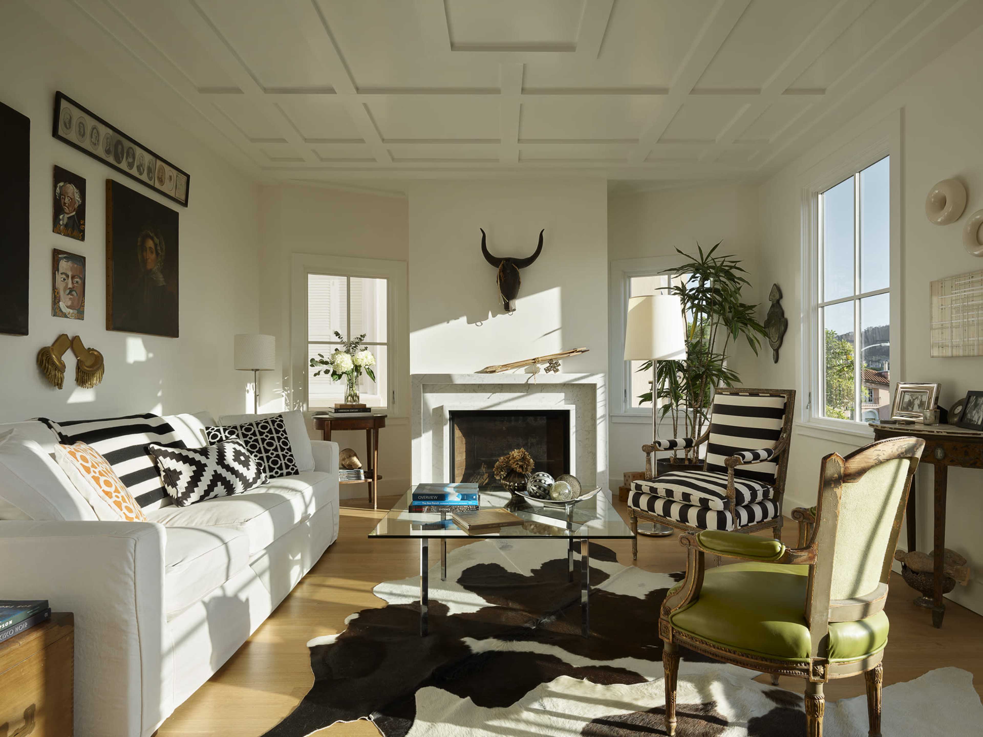 The living room features a white couch, striped chairs, a glass coffee table, and a fireplace, with an assortment of artwork on the walls and a cowhide rug on the floor.