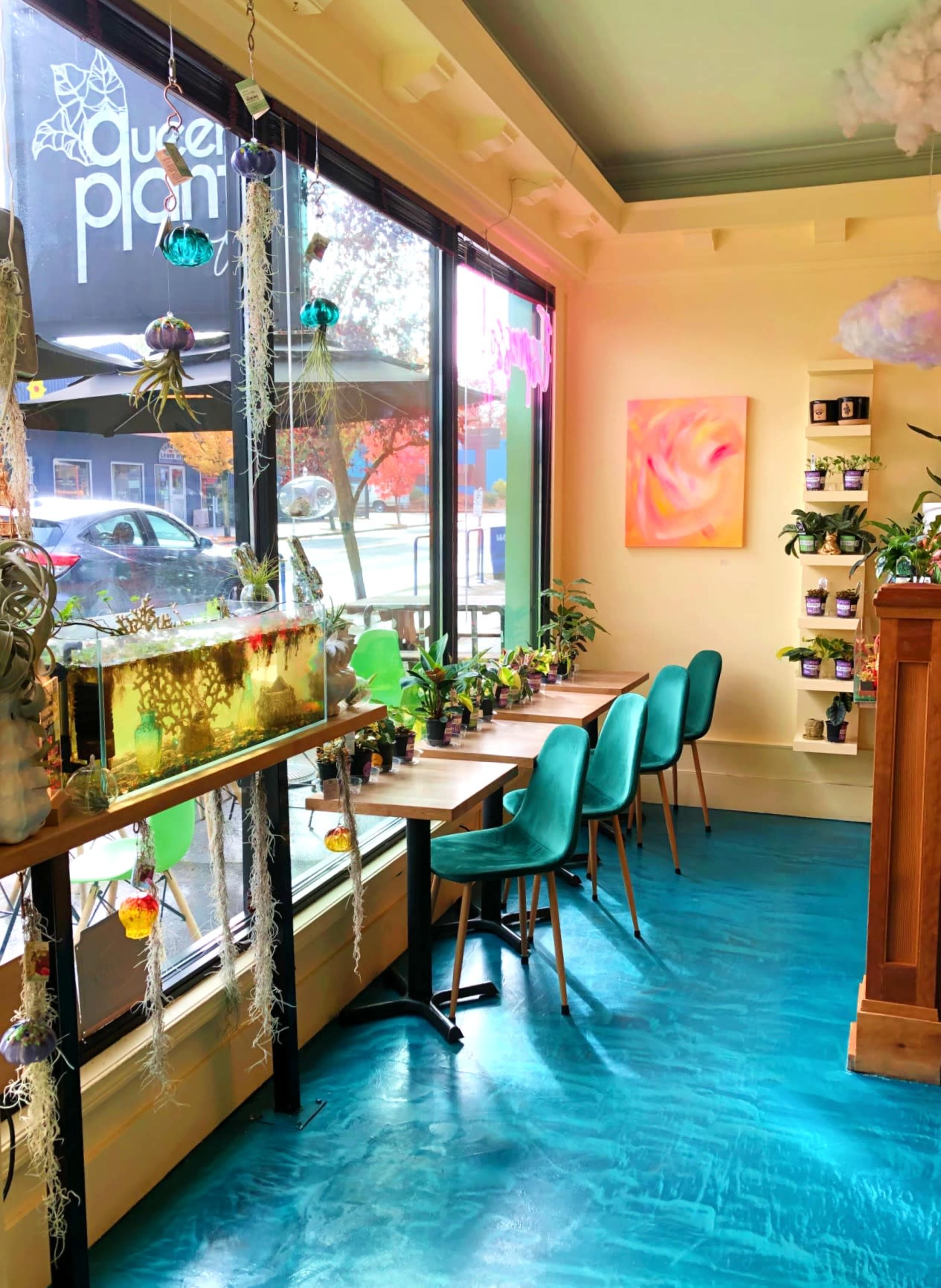 The image shows a bright cafe interior with tables by large windows, an aquarium, and plants on display.
