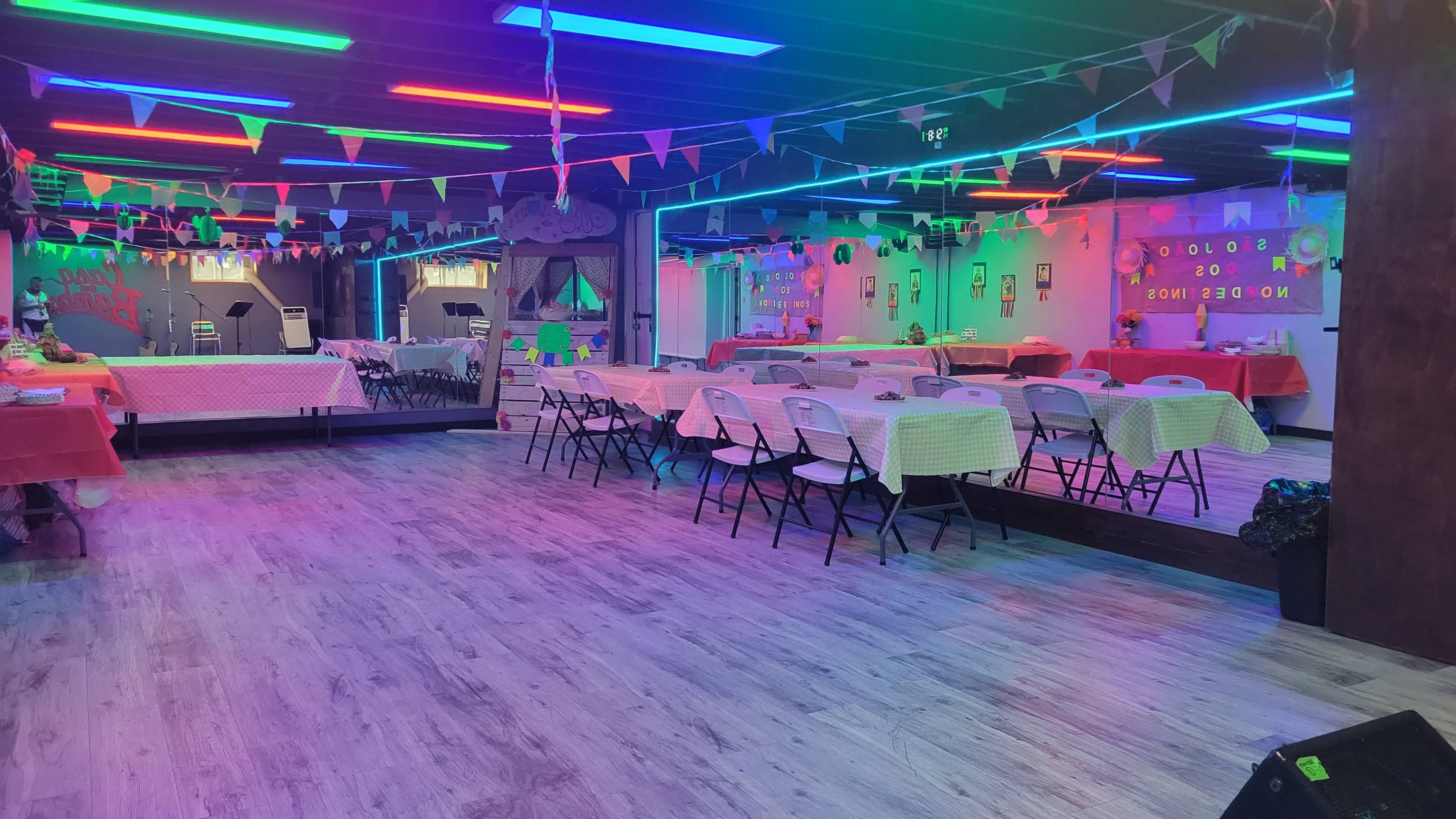 The image shows a brightly lit event space with colorful lights and tables covered in checkered tablecloths, arranged for a gathering.