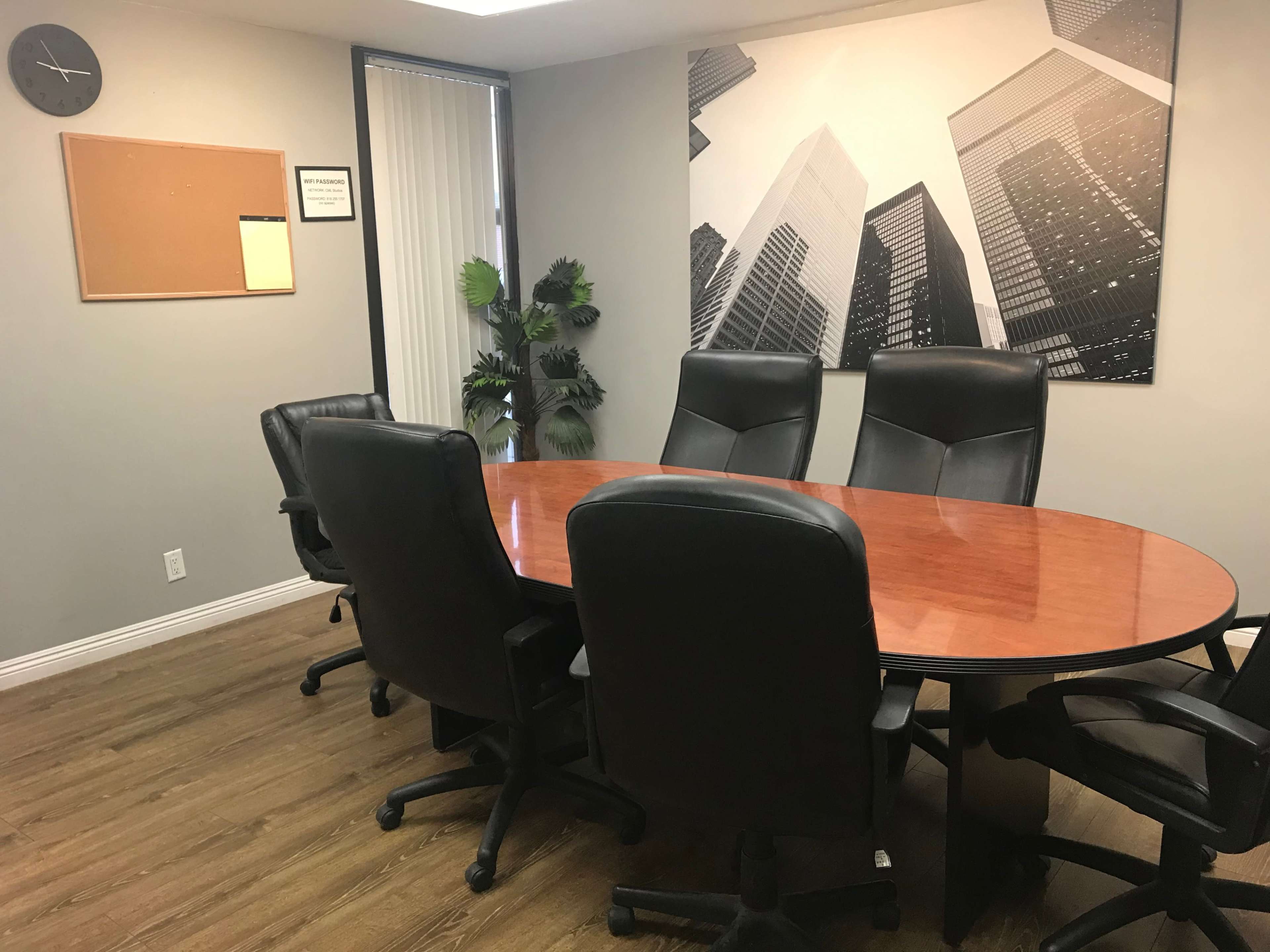 A conference room featuring an oval wooden table surrounded by black leather chairs and a large black-and-white cityscape photograph on the wall.