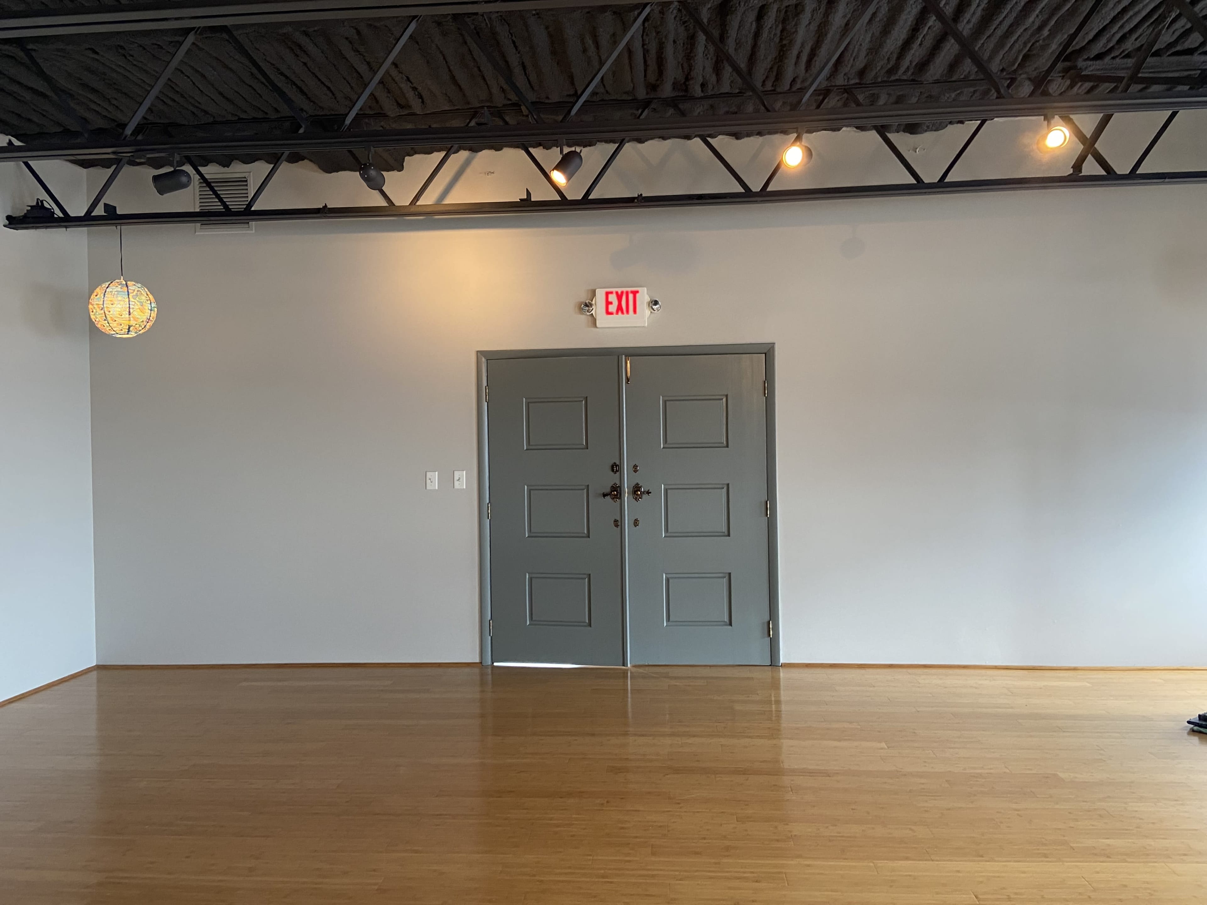 A simple room features a pair of gray double doors on a light-colored wall, with a pendant light and exposed ceiling beams above.