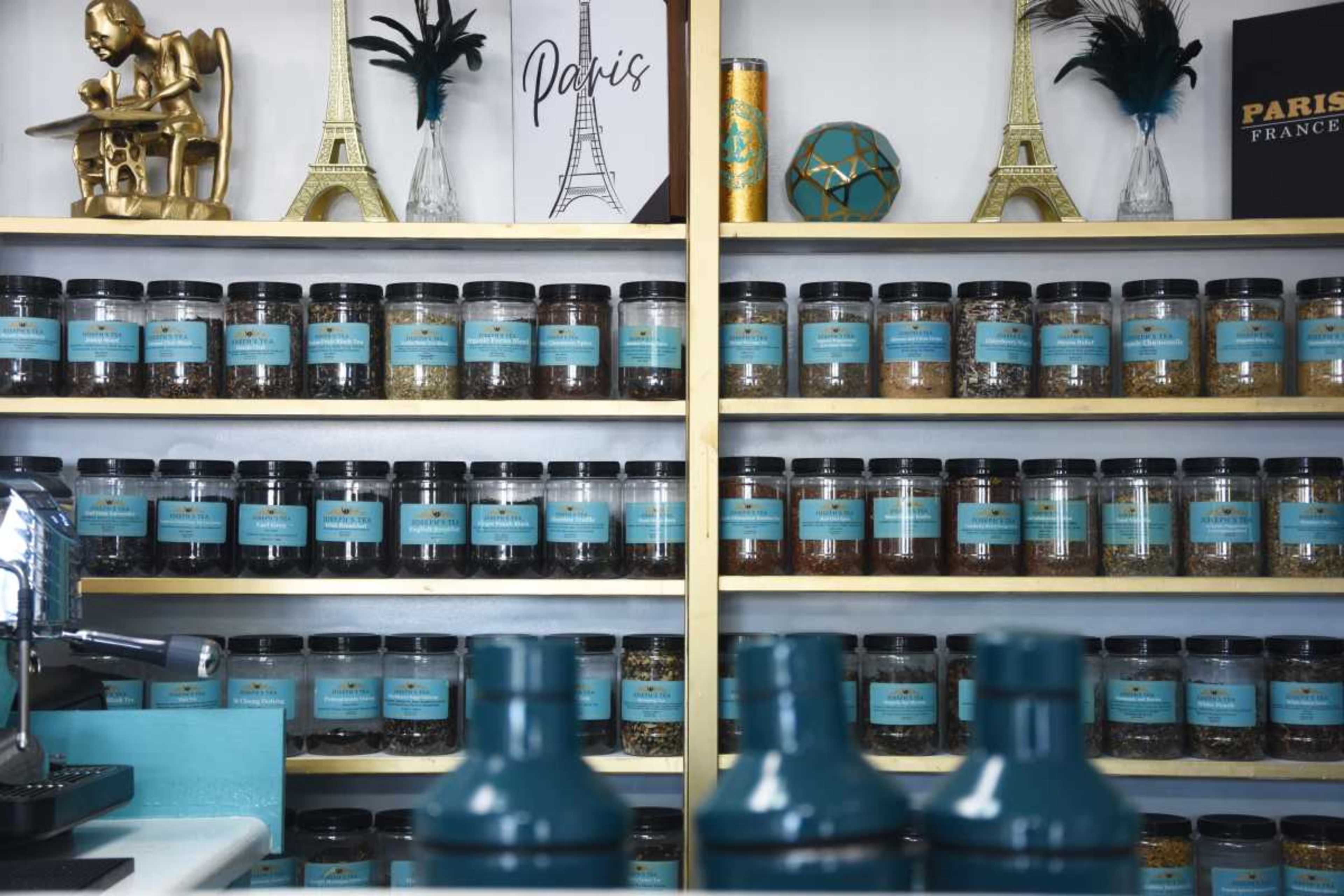 A shelf displays jars of various loose teas, organized neatly beneath decorative items and a sign featuring the Eiffel Tower.