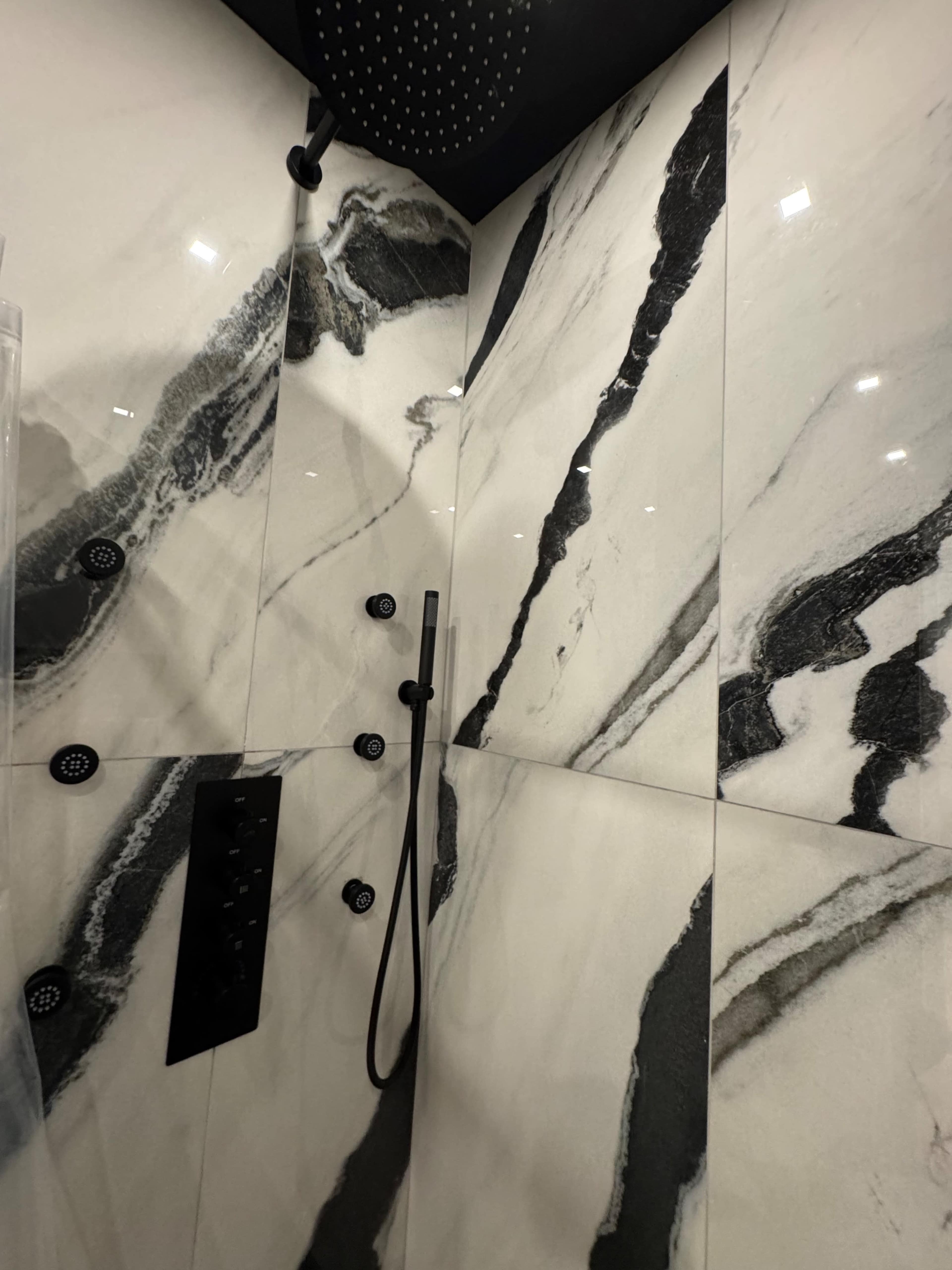 The image shows a modern shower featuring sleek black and white marble walls and a rain showerhead.