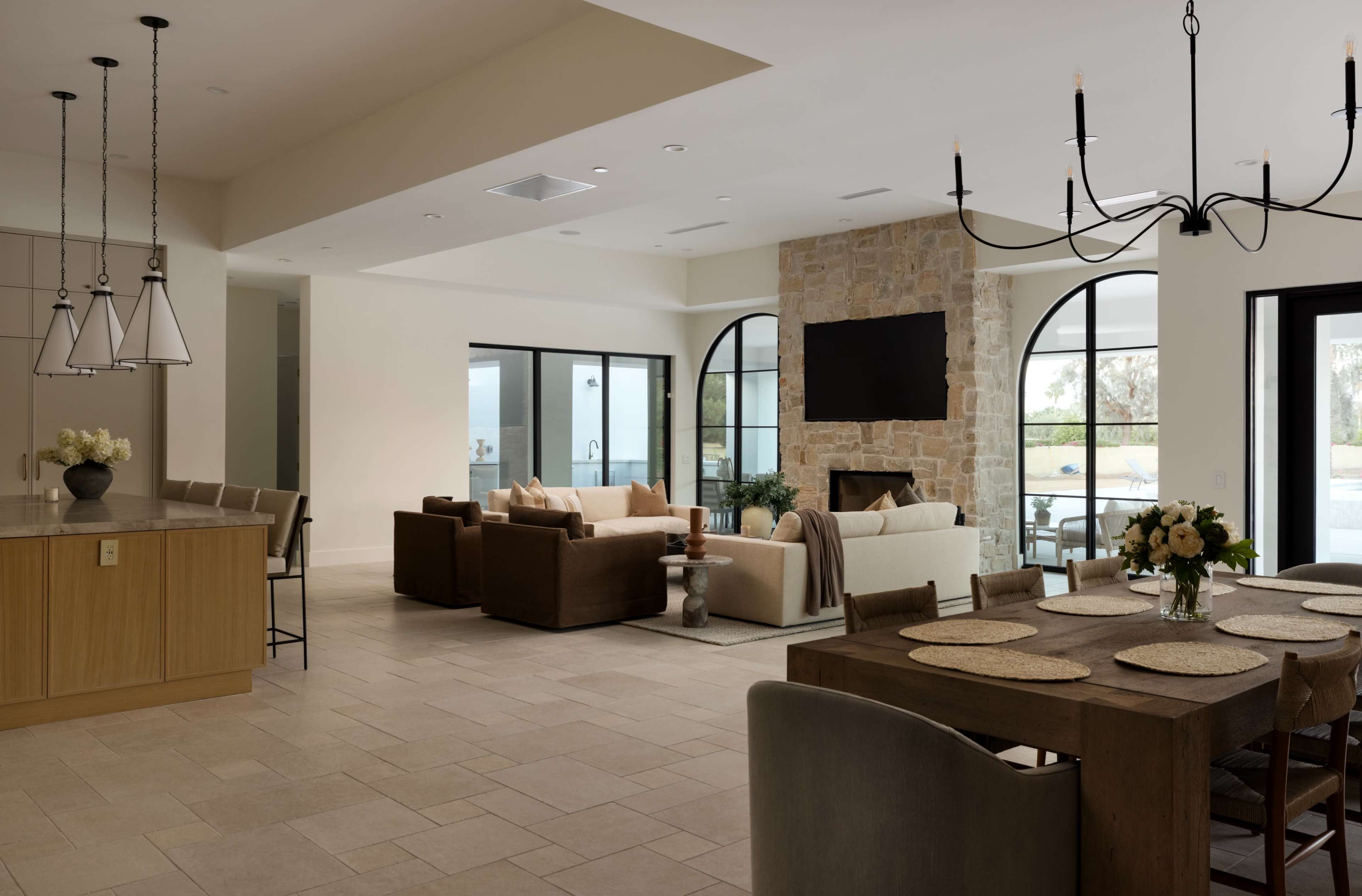 The image shows an open-concept living space with a dining area, a kitchen island, and a cozy seating arrangement near a stone fireplace and a large screen.