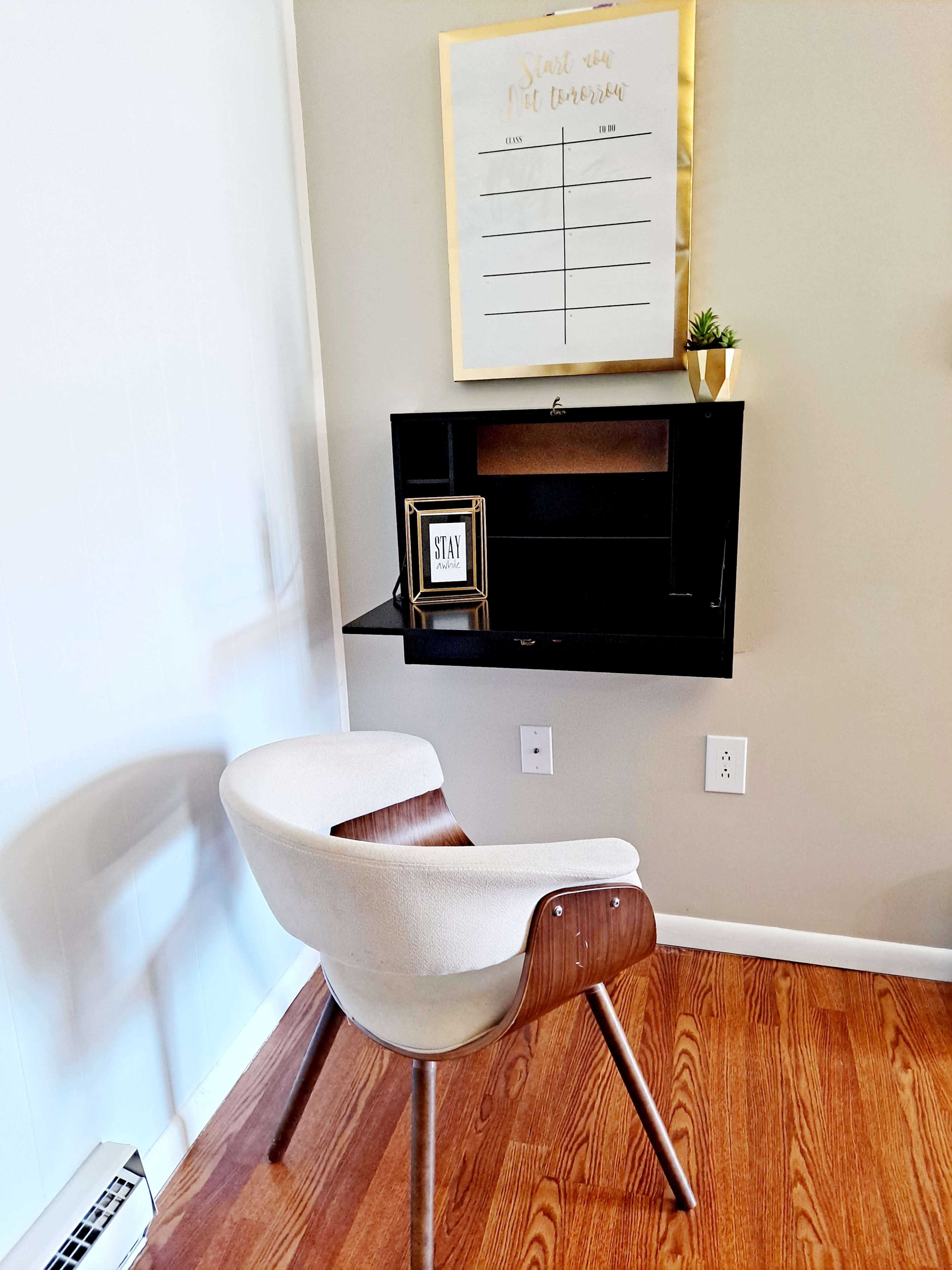A modern chair is positioned next to a wall-mounted desk with a small plant and a framed sign on it.