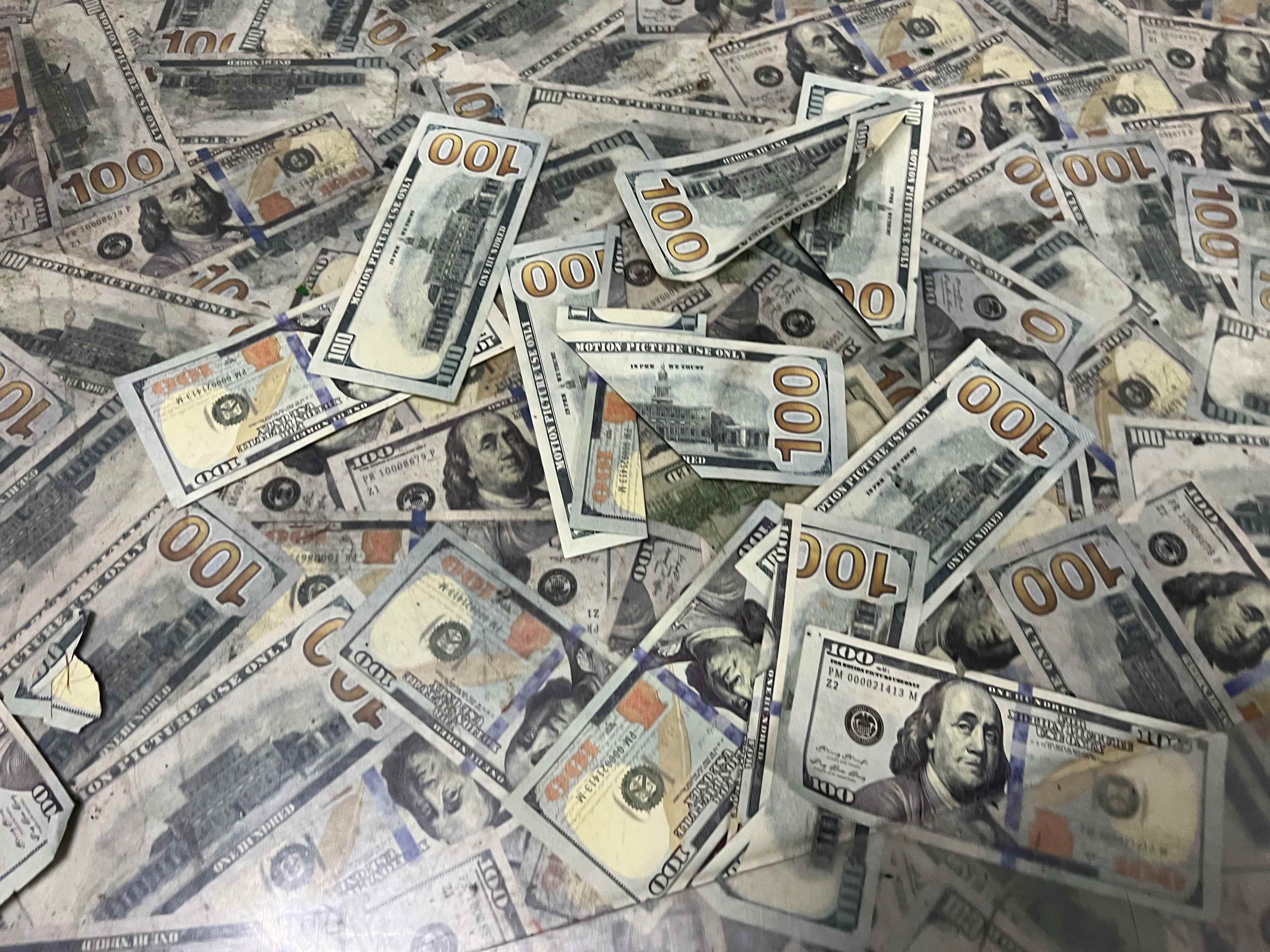 The image shows a scattered arrangement of one hundred dollar bills on a flat surface.