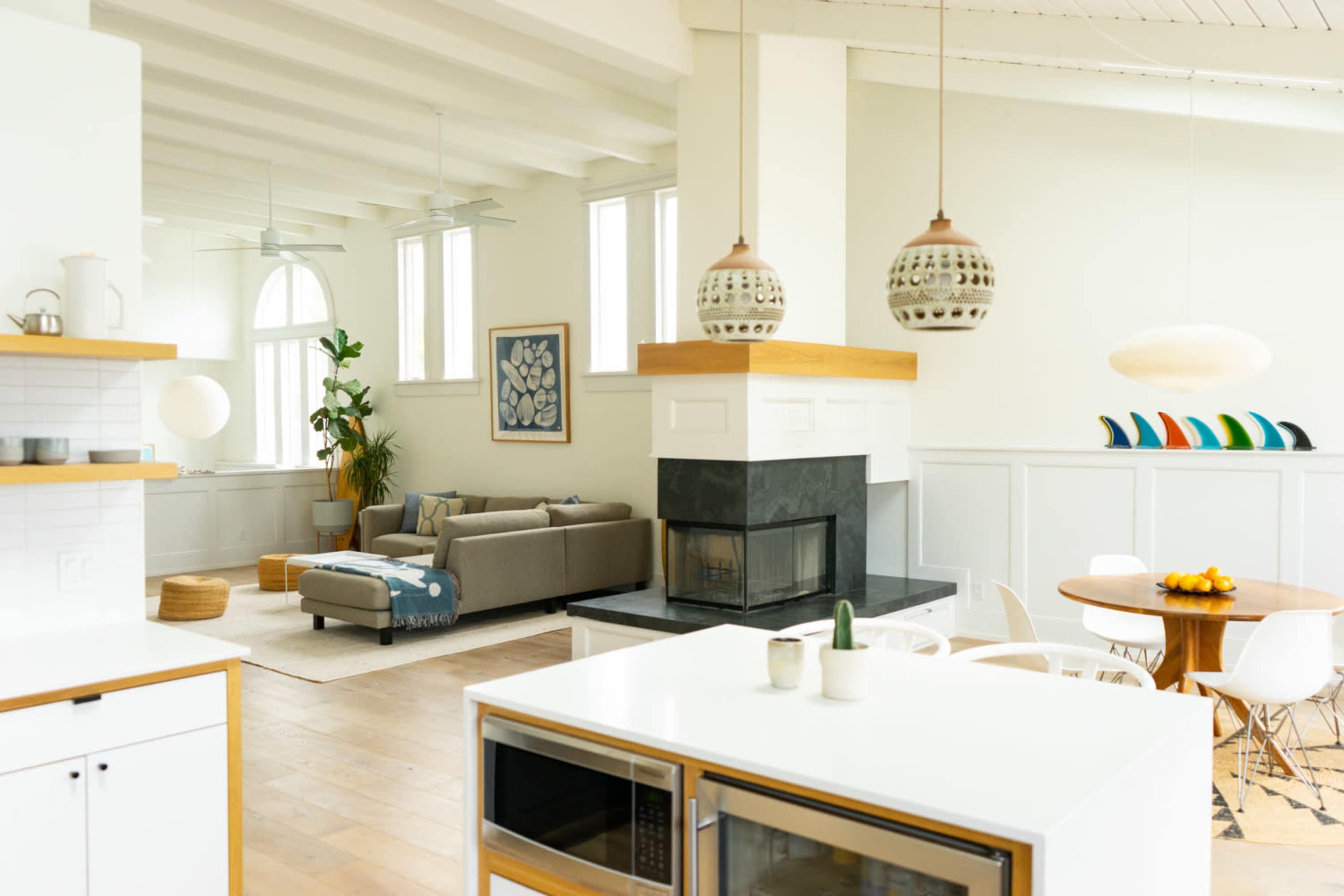 A modern open-concept living space with a kitchen, dining area, and a comfortable seating area, featuring large windows and decorative lighting.