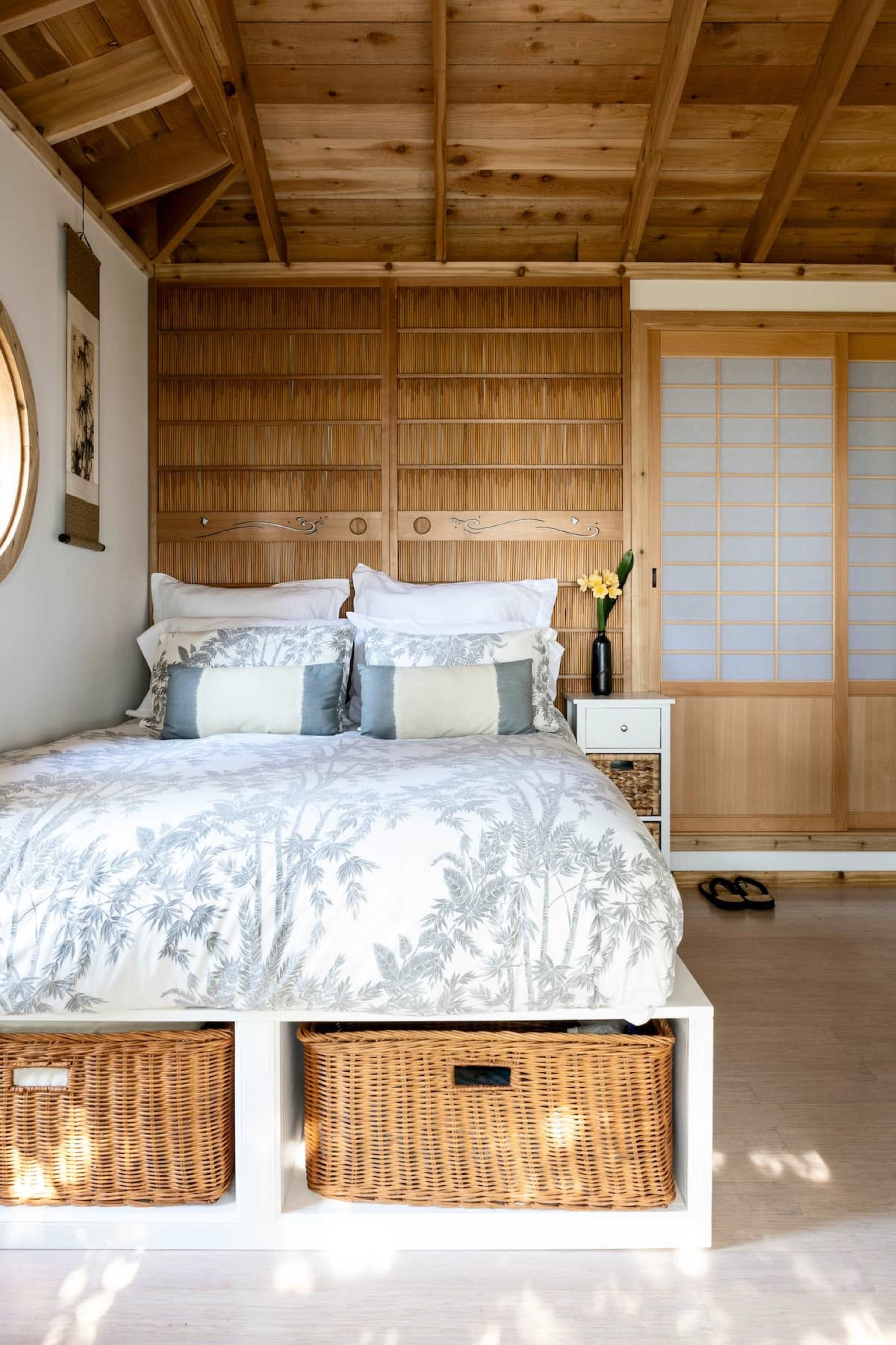 A neatly arranged bedroom featuring a centrally positioned bed with a patterned duvet, wooden walls, and minimalistic furniture.