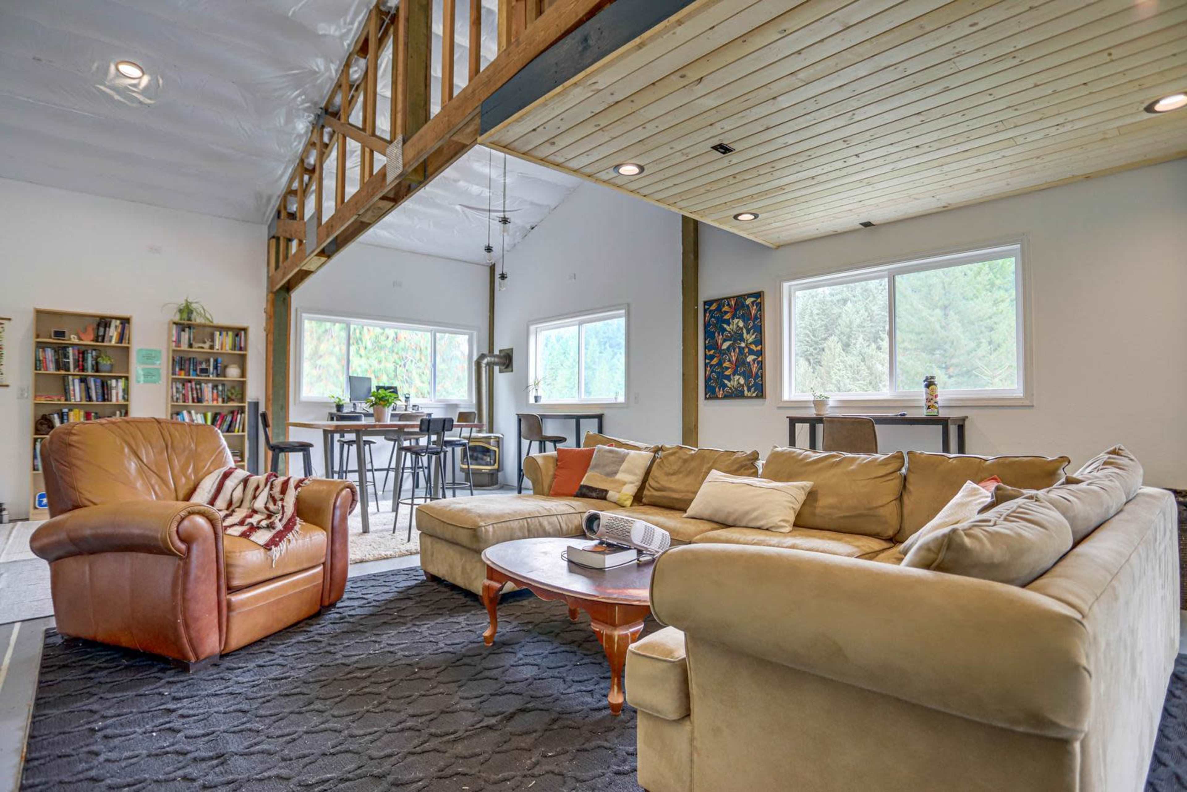 A spacious living area featuring a large sofa, an armchair, a coffee table, and a bookshelf, with large windows that provide natural light.