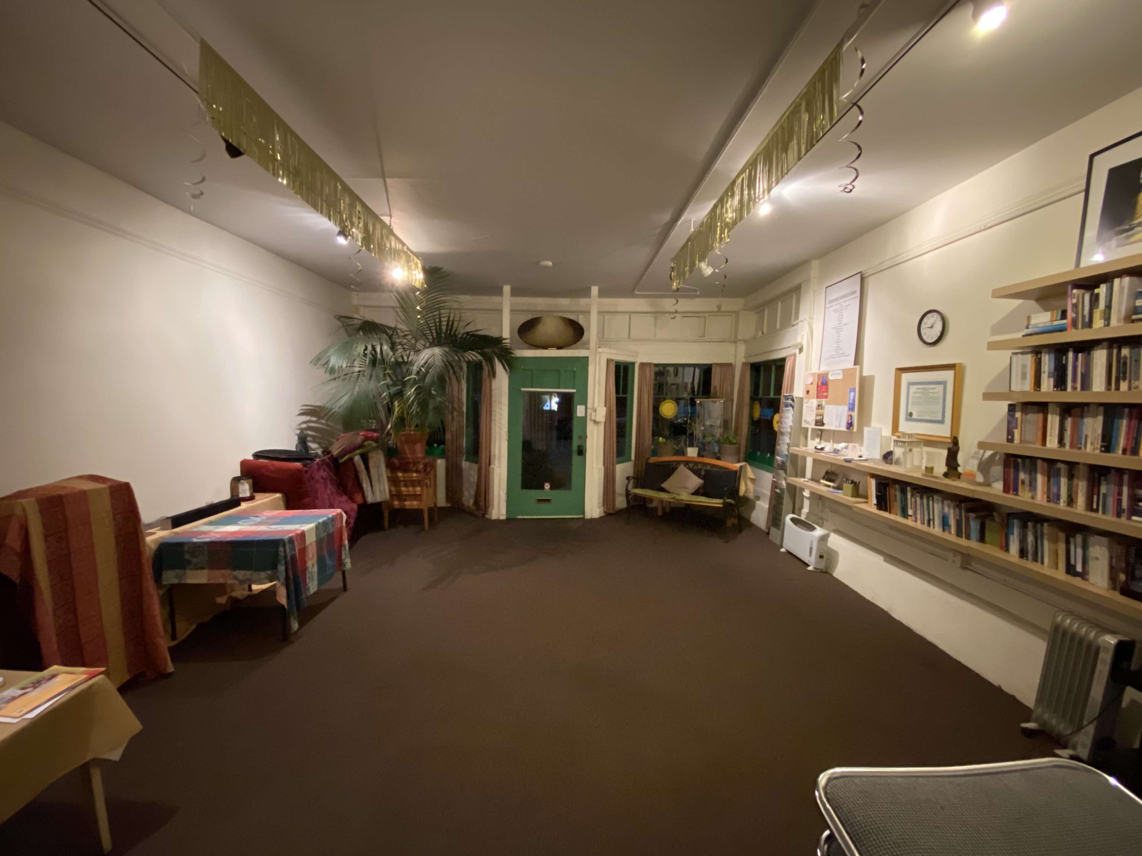 A spacious, dimly lit room with a seating area, a bookshelf along the wall, and green doors leading to another area.