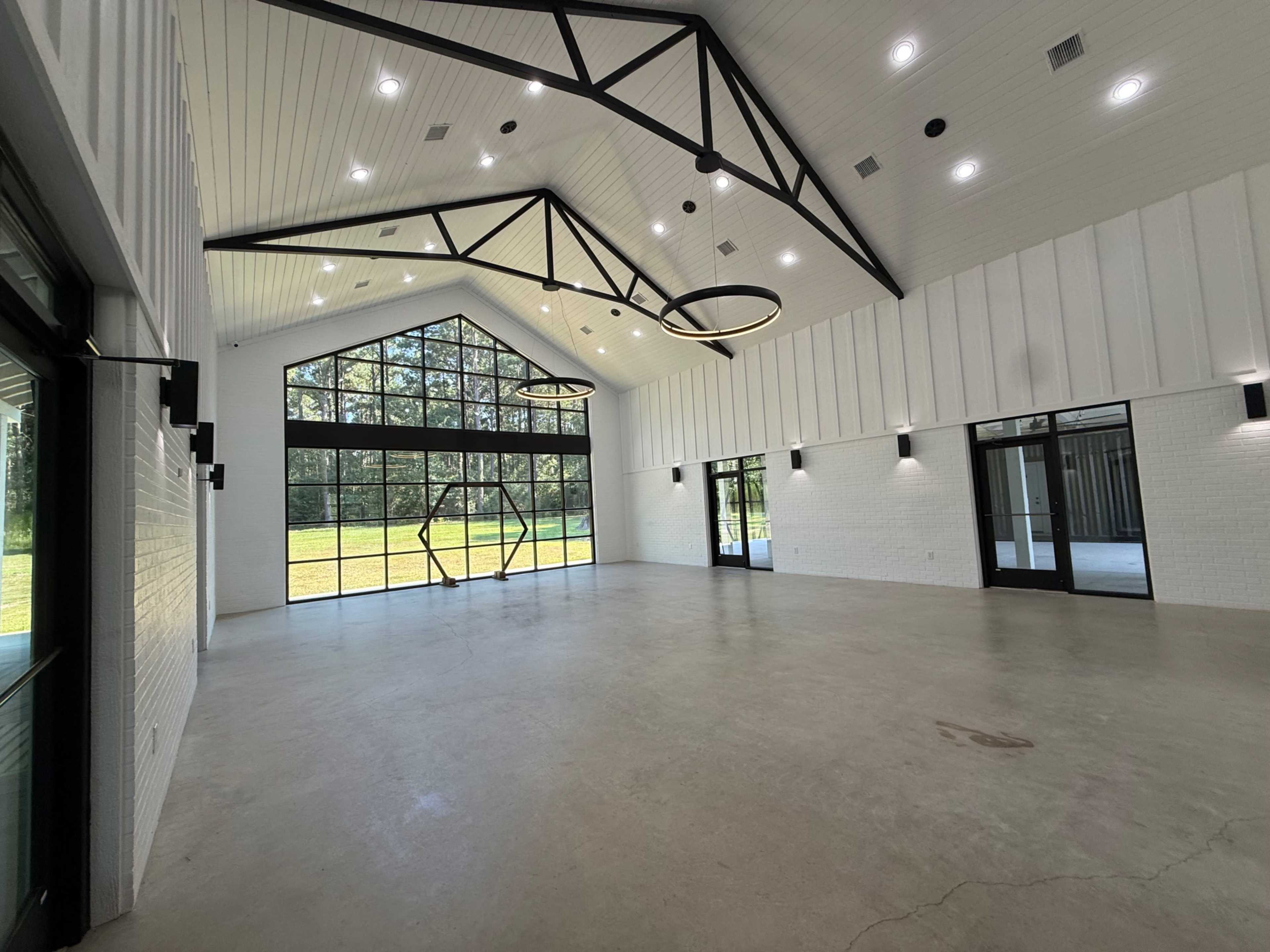 The image shows a spacious interior of a modern building with large windows, high ceilings, and minimalist design elements.