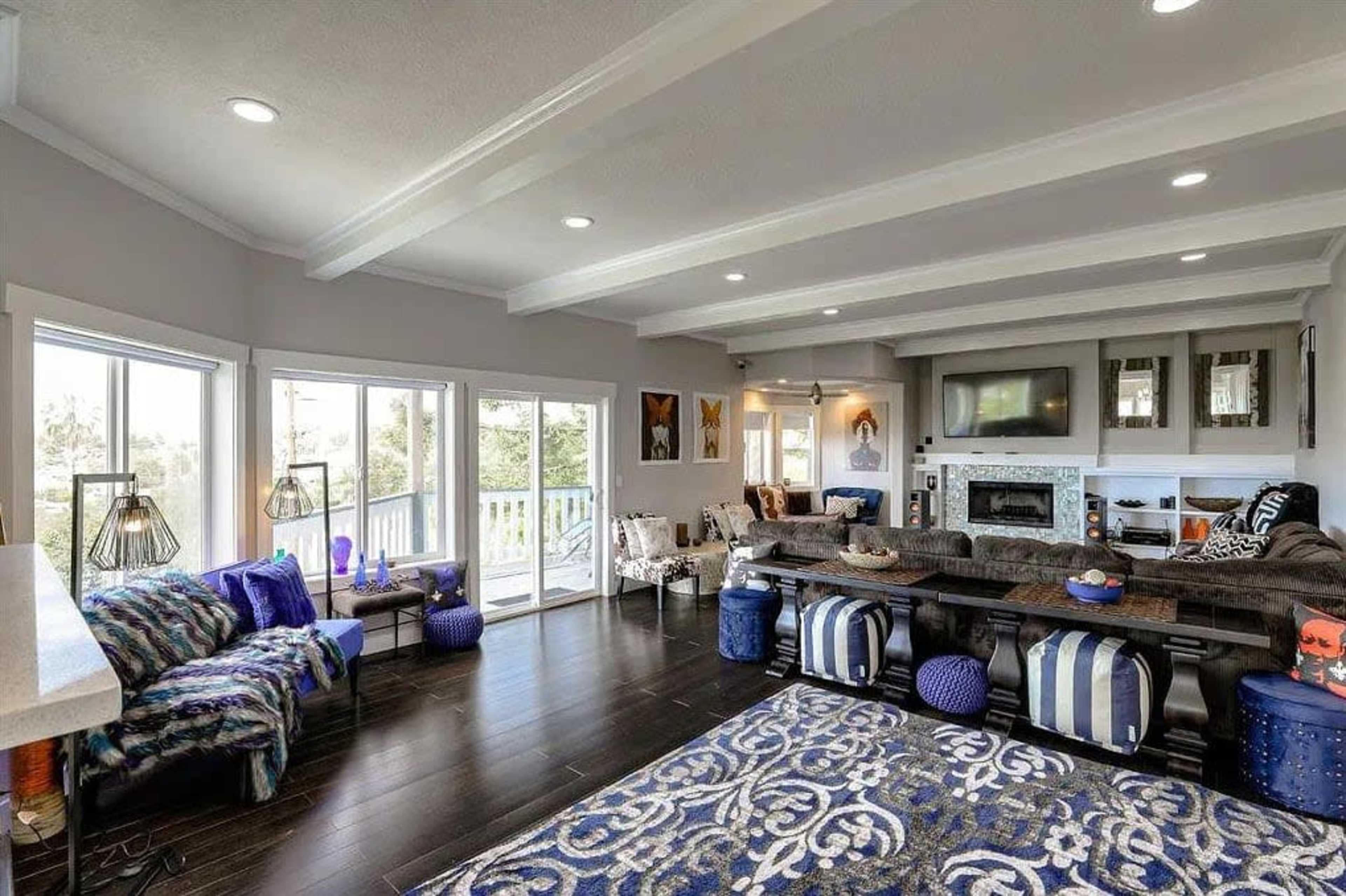 The interior of a spacious living room features a sectional sofa, a large area rug, and multiple windows allowing natural light.