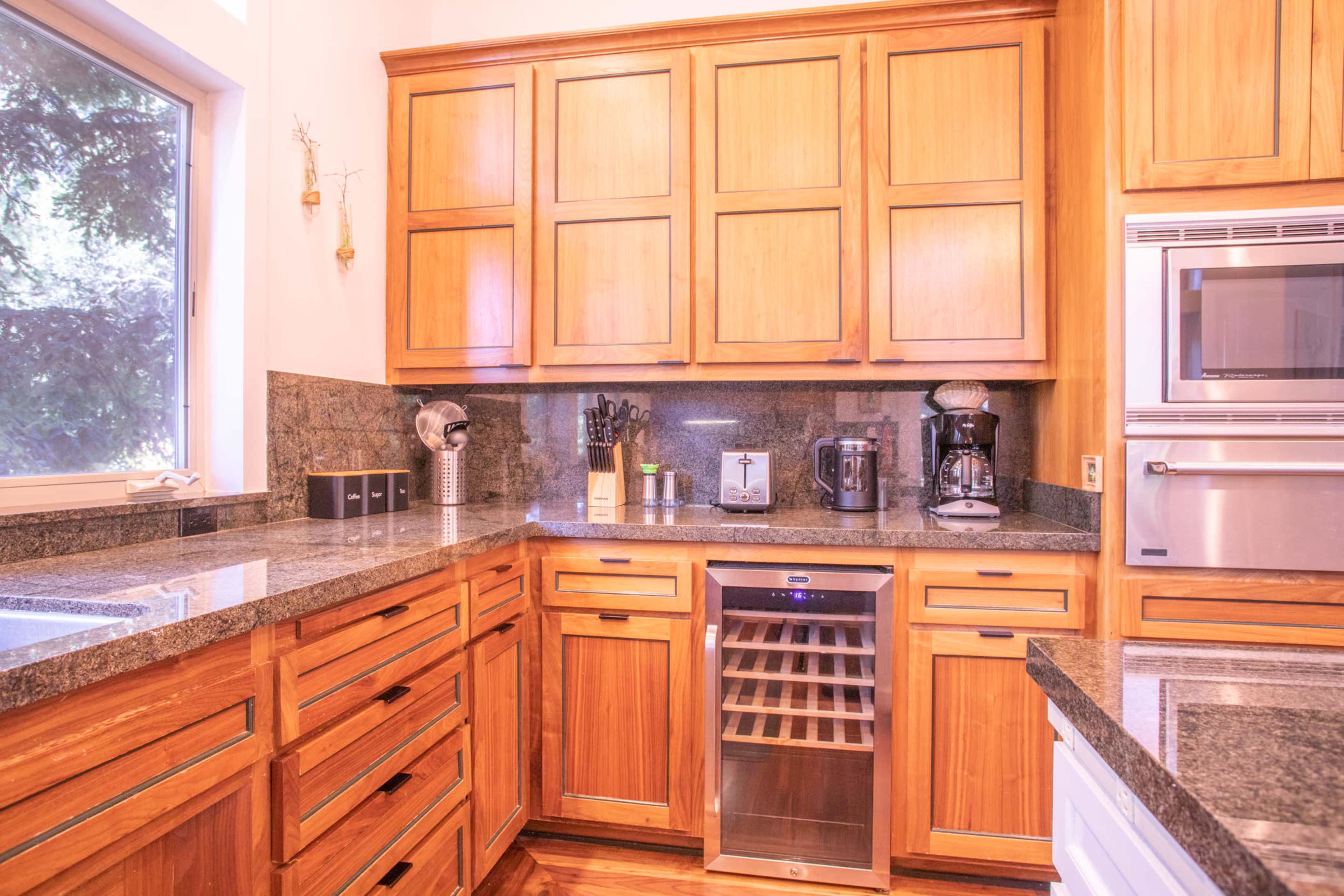 A modern kitchen with wooden cabinetry, a granite countertop, and appliances including a coffee maker and a wine cooler.