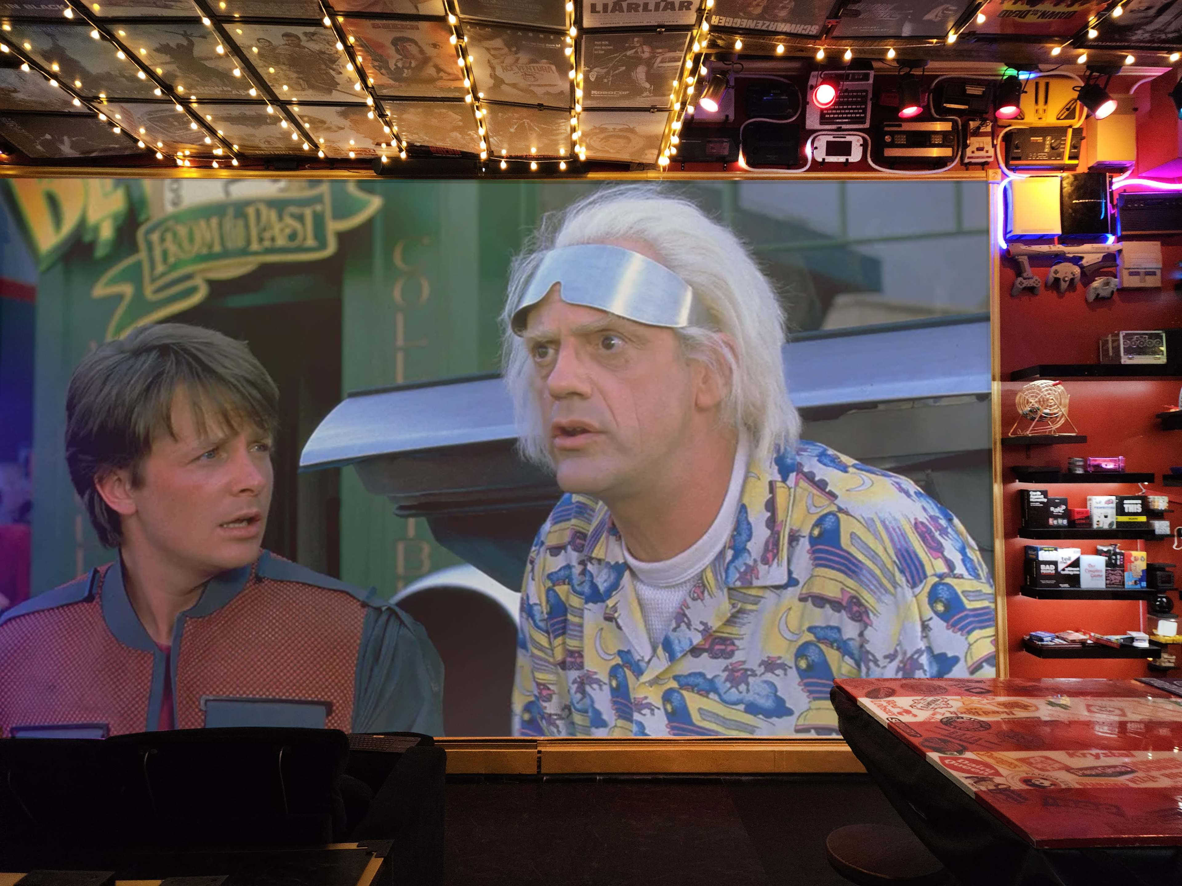 A scene from a movie is projected on a wall in a brightly lit room decorated with memorabilia and retro items.