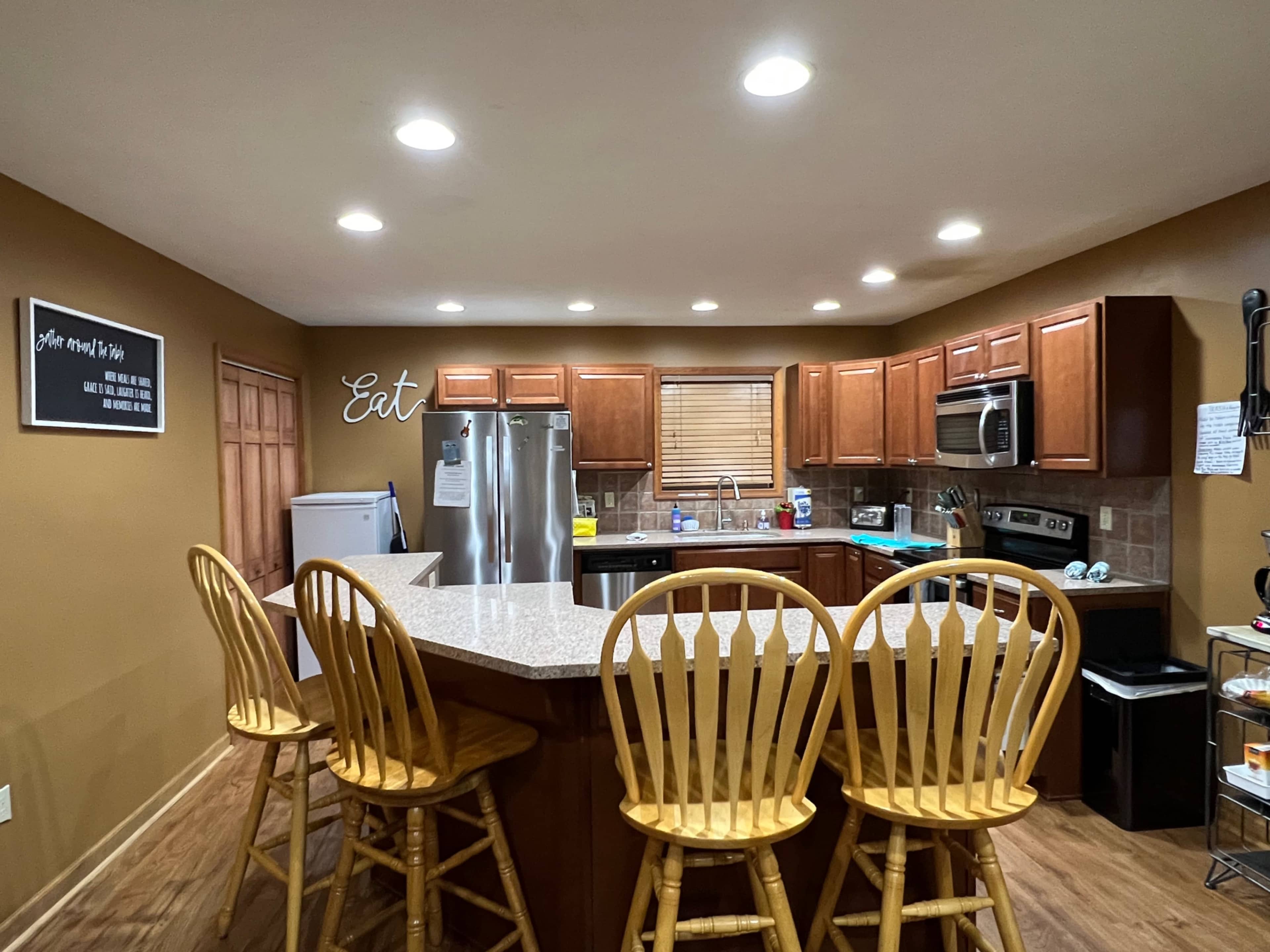 The kitchen features wooden cabinets, stainless steel appliances, and a large island with four wooden bar stools.