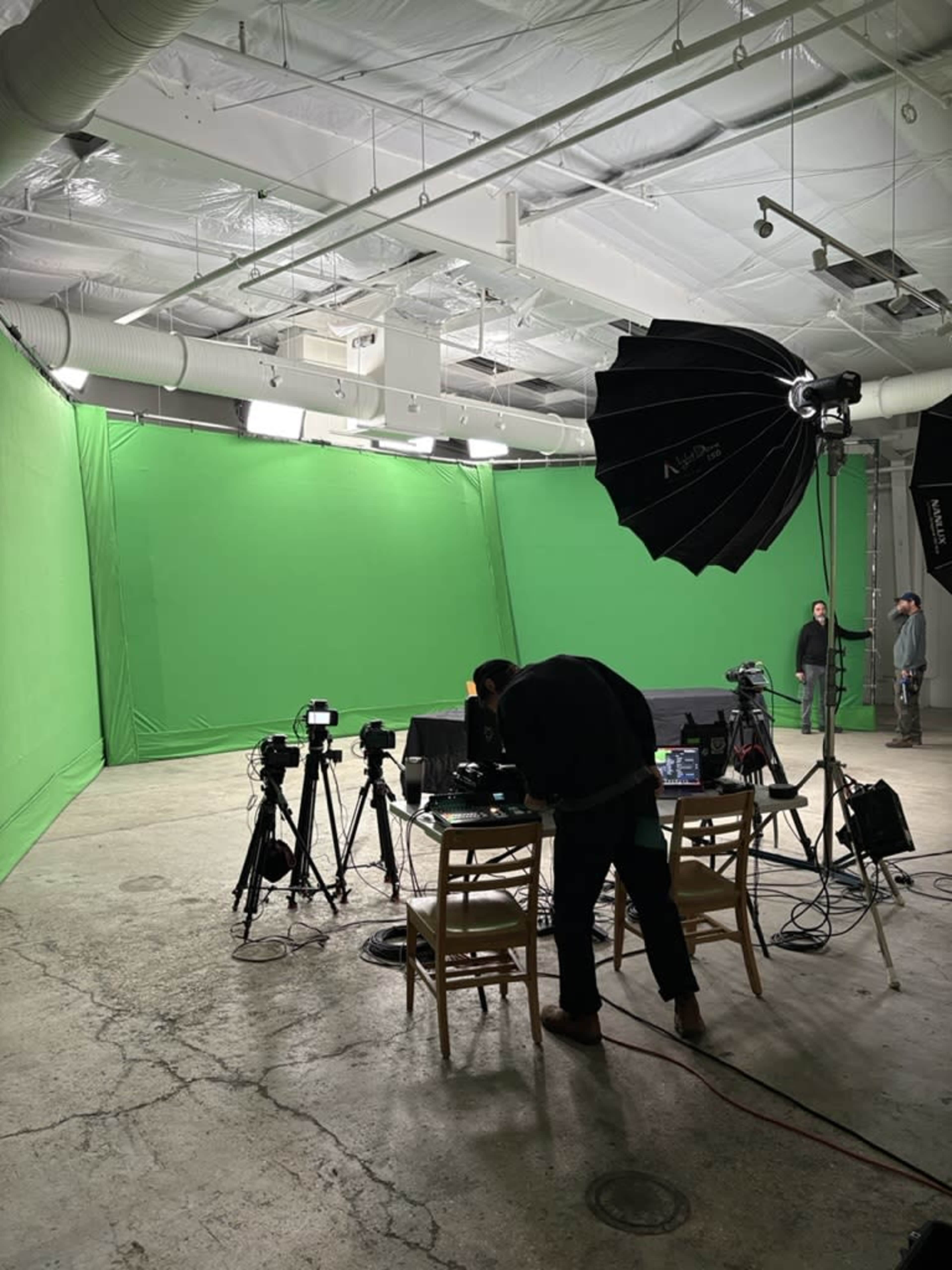 A person is setting up equipment in a studio with green screens and various cameras.