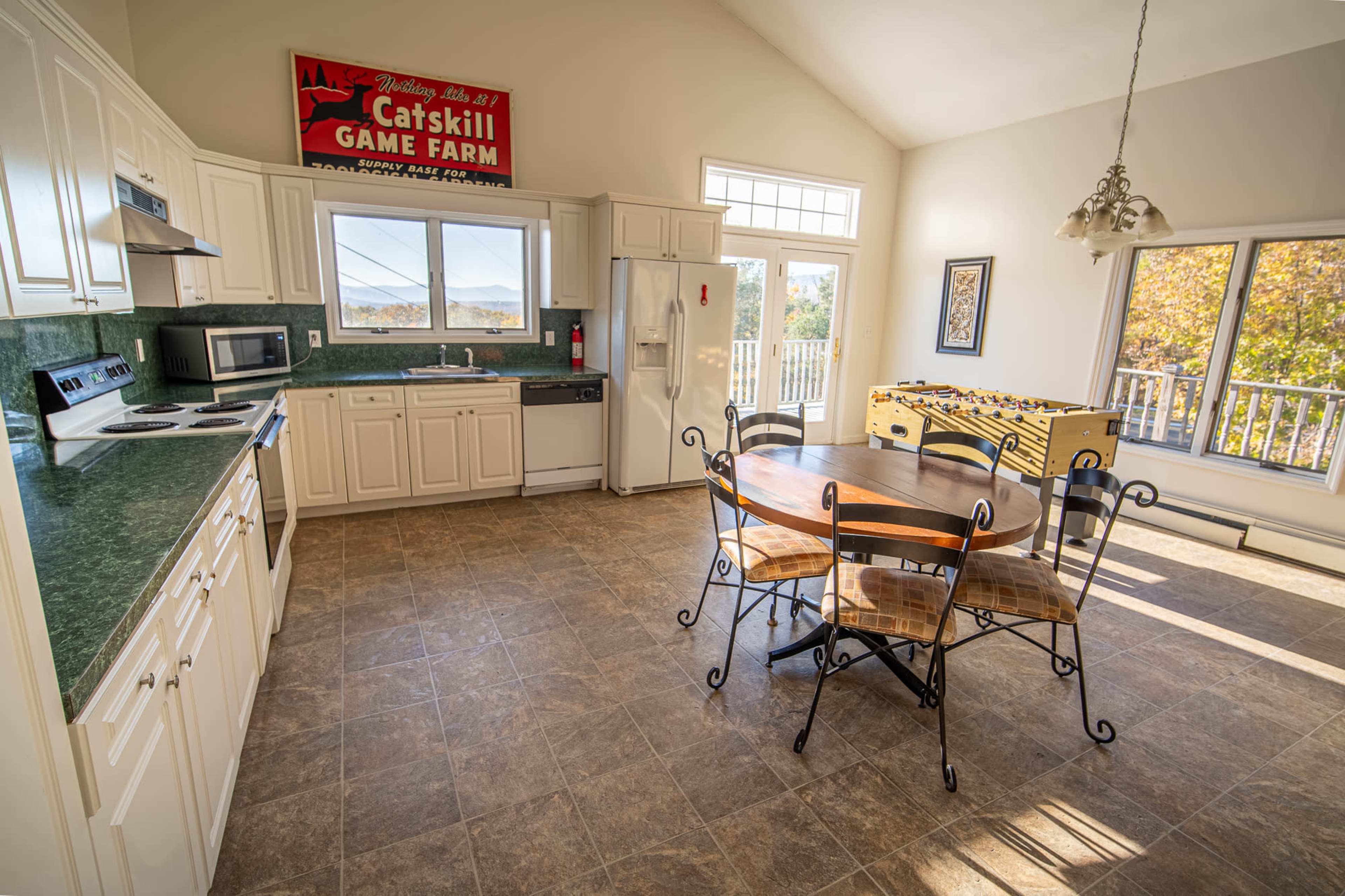 A bright kitchen features white cabinetry, a green countertop, and a round dining table surrounded by metal and wooden chairs.