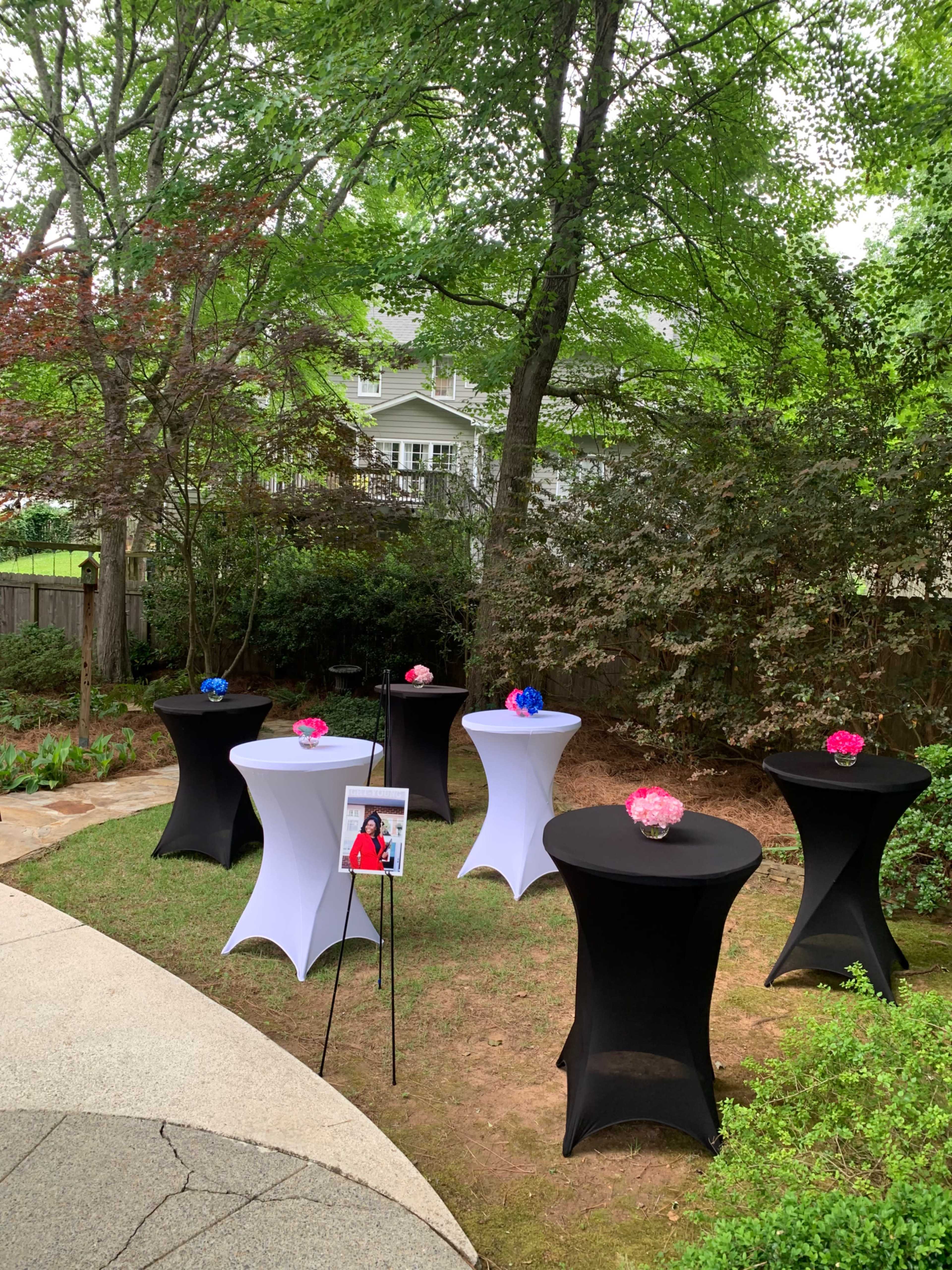 The image shows several cocktail tables with colorful floral centerpieces arranged in a garden setting.