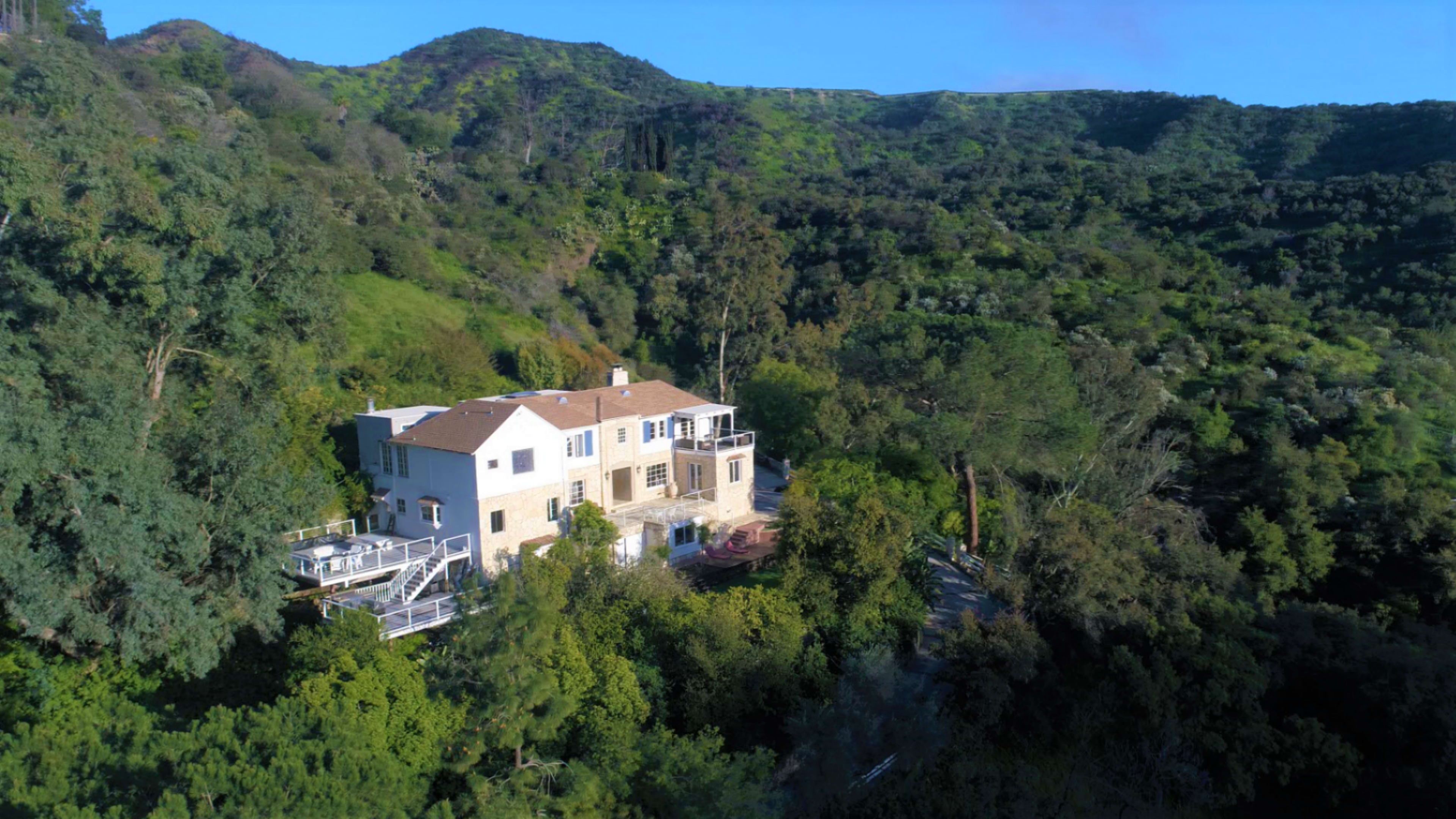 A large house is situated amidst lush greenery on a hillside.