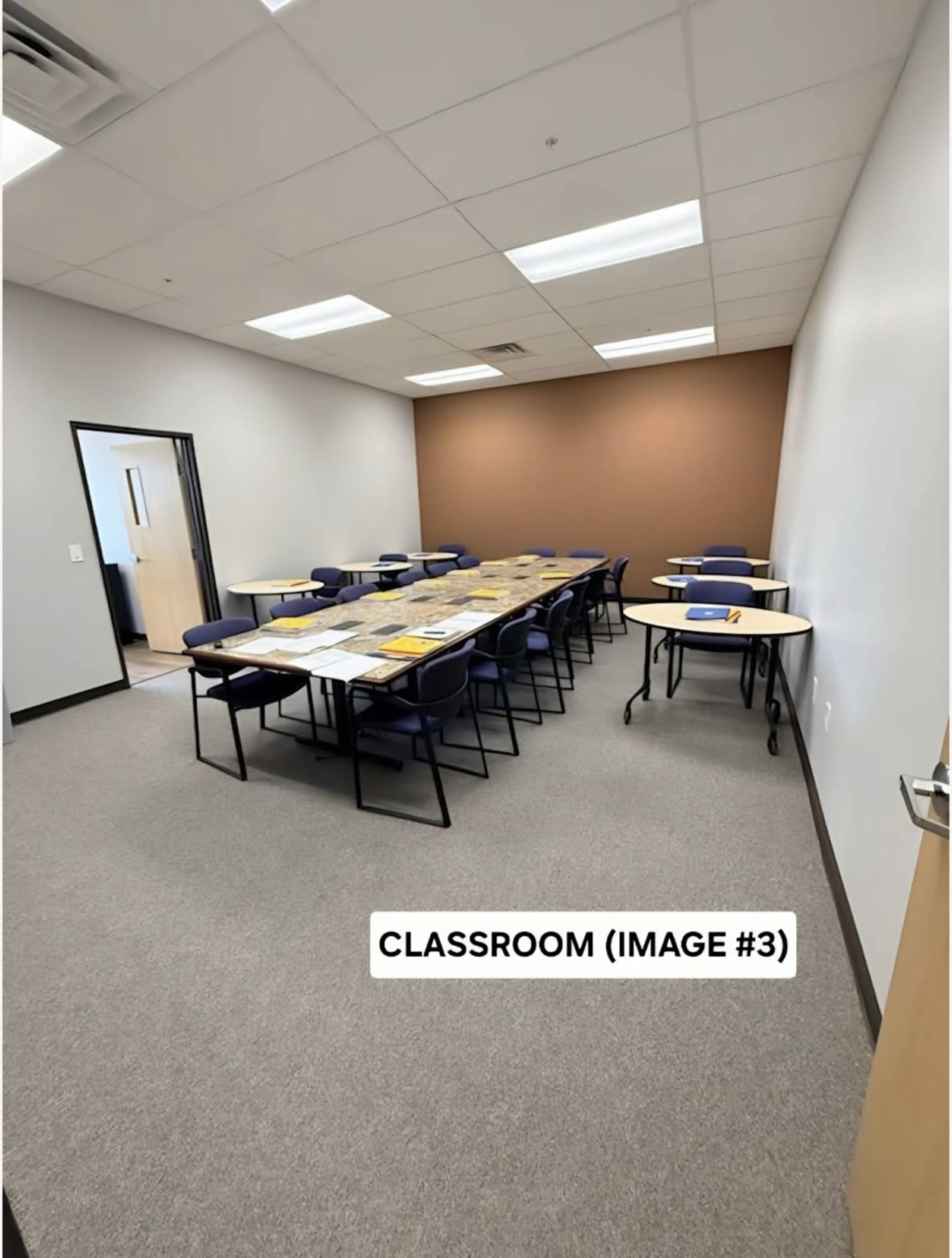 The image shows a classroom with rows of desks arranged in a U-shape, surrounded by gray walls and a brown accent wall.