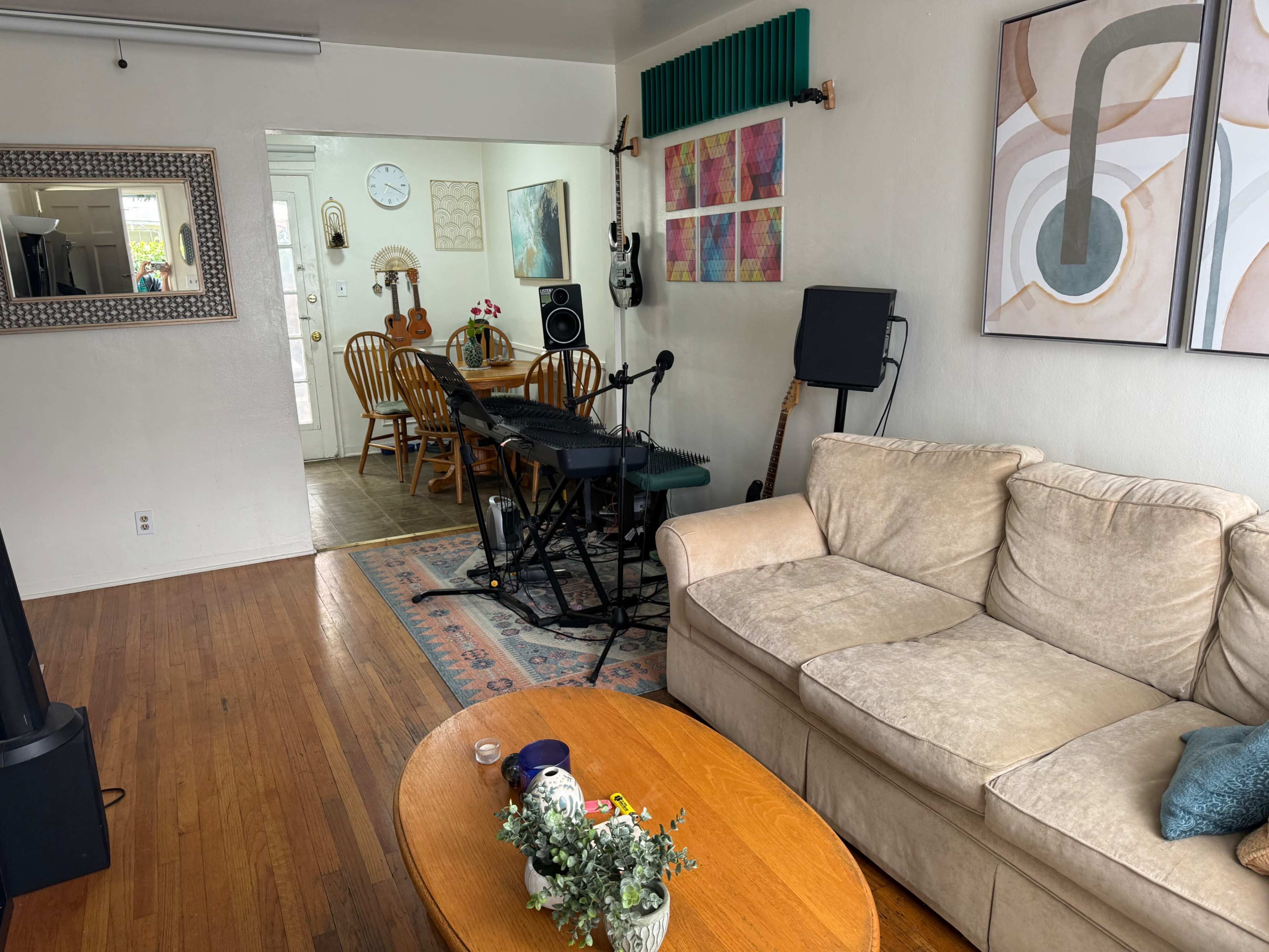 The image shows a living room with a beige couch, a wooden coffee table, and a keyboard set up near a dining area that has wooden chairs and a table.