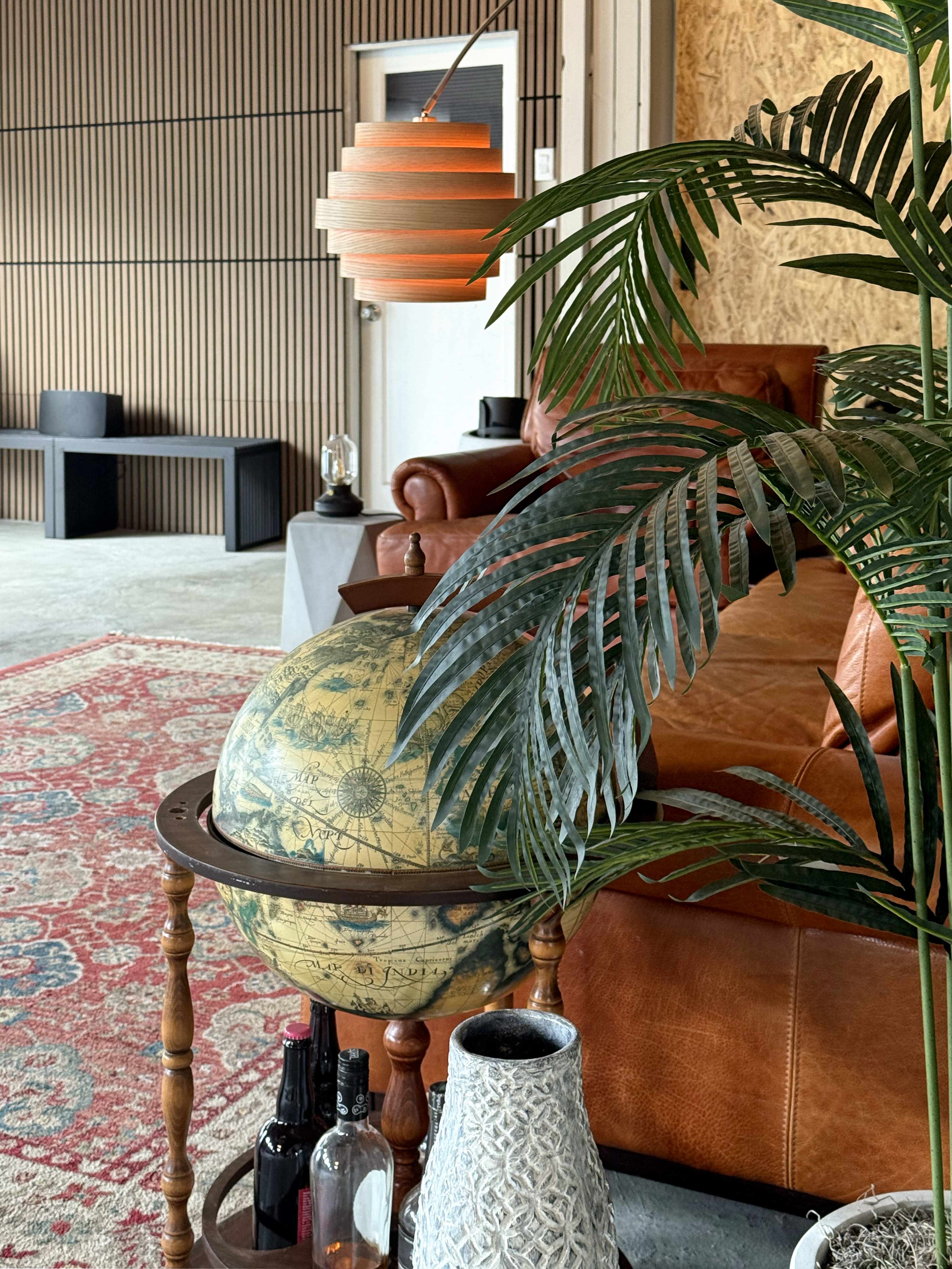 The image features a vintage globe on a wooden stand, a decorative plant, and a modern light fixture in a cozy seating area with a leather couch and an ornate rug.