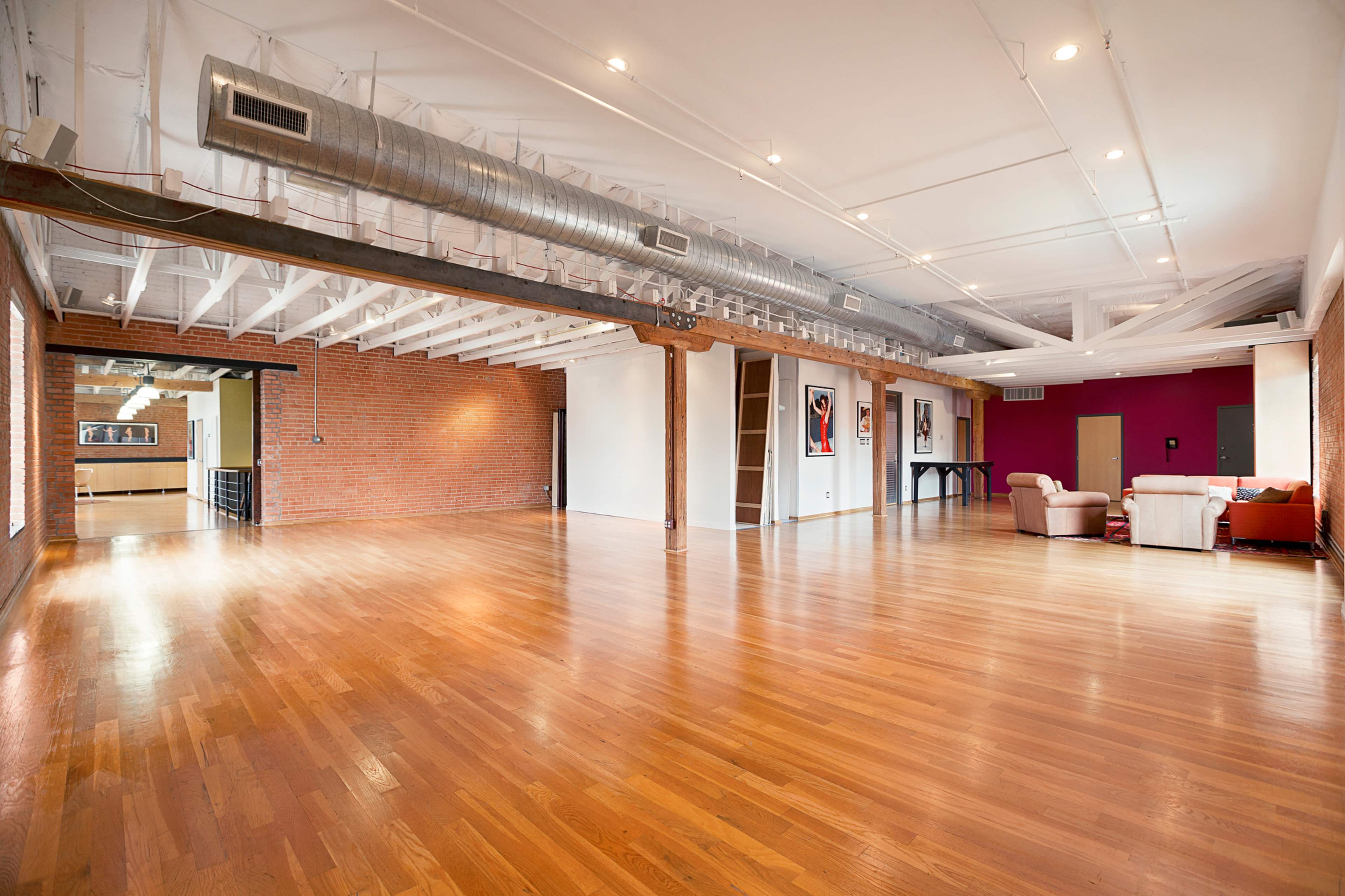A spacious room with hardwood floors, exposed brick walls, and a combination of modern and traditional furnishings.