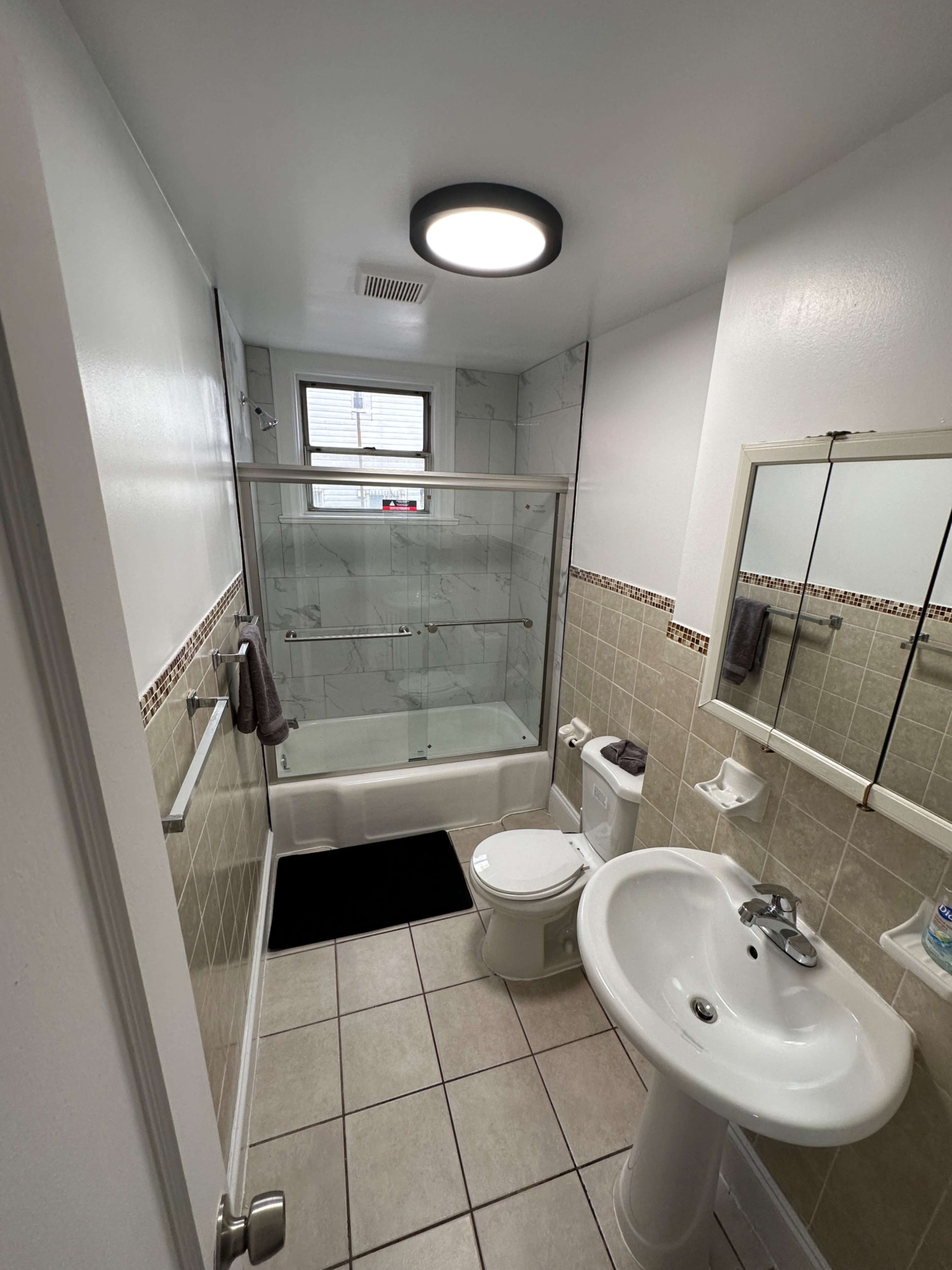 A clean, compact bathroom featuring a shower with a glass door, a toilet, a sink, and tiled flooring.
