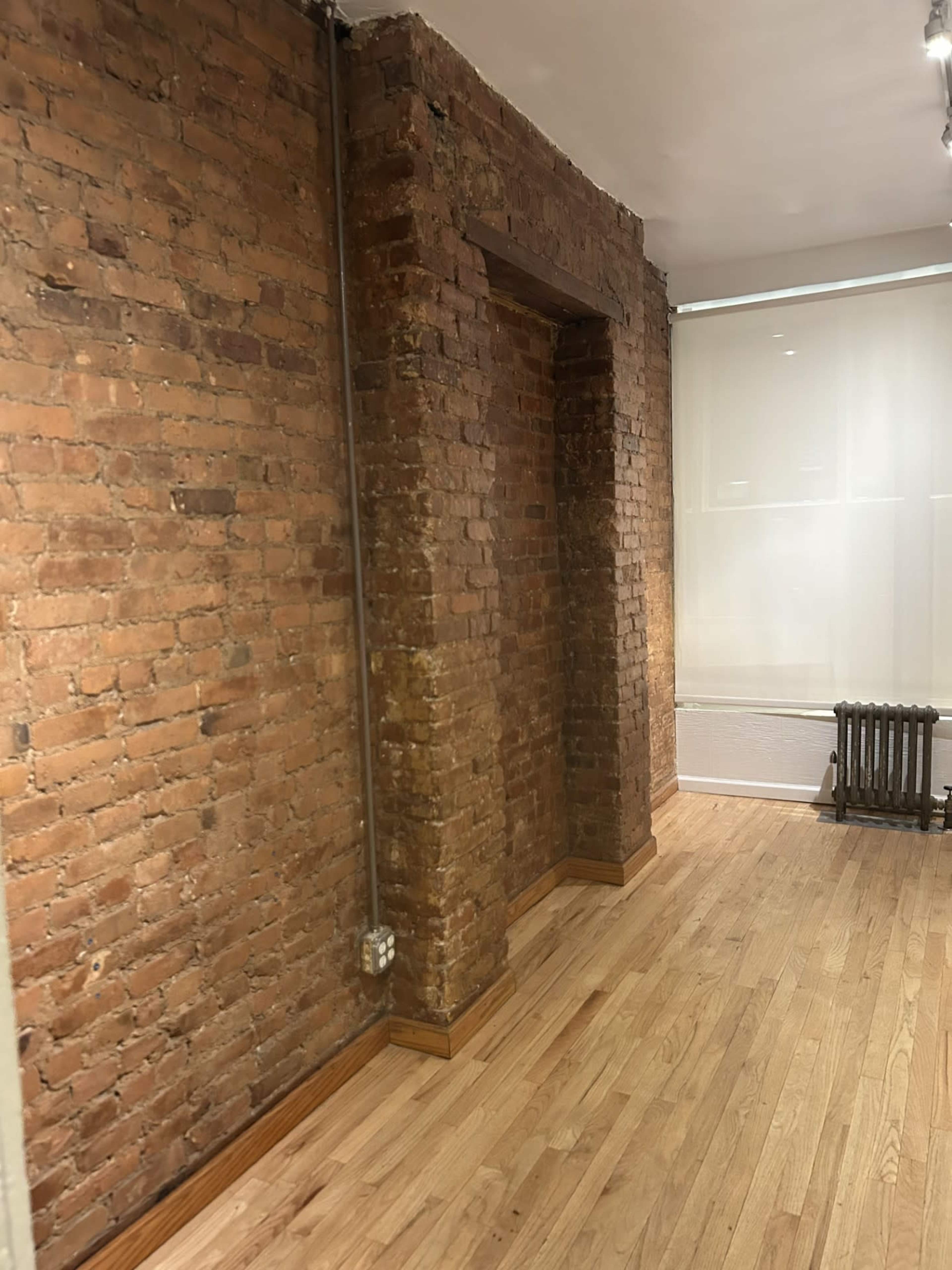 The image shows an interior space with exposed brick walls, wooden flooring, and a radiator along one side.