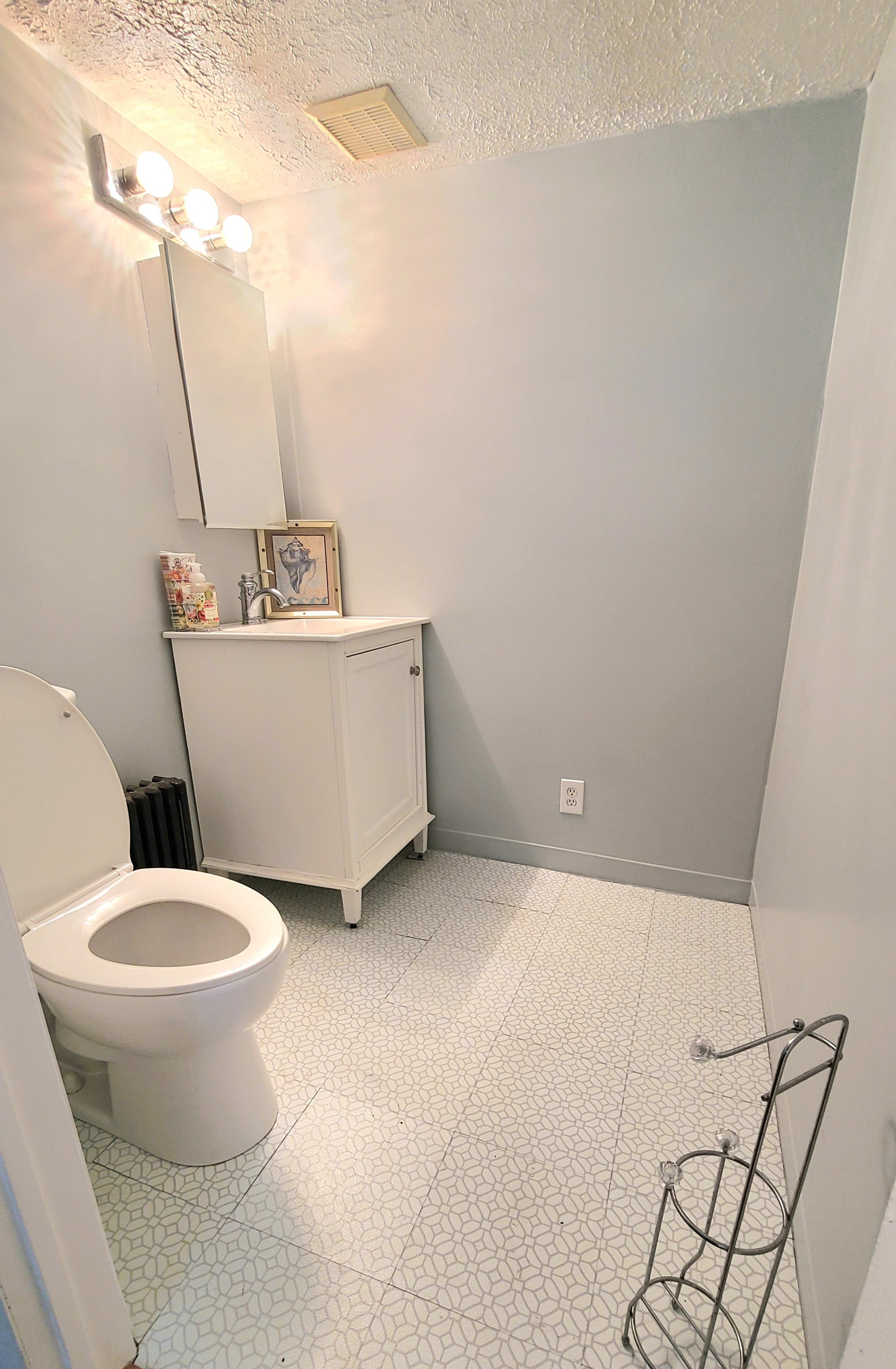 A small bathroom featuring a white toilet, a cabinet with a sink, a mirror, and patterned flooring.