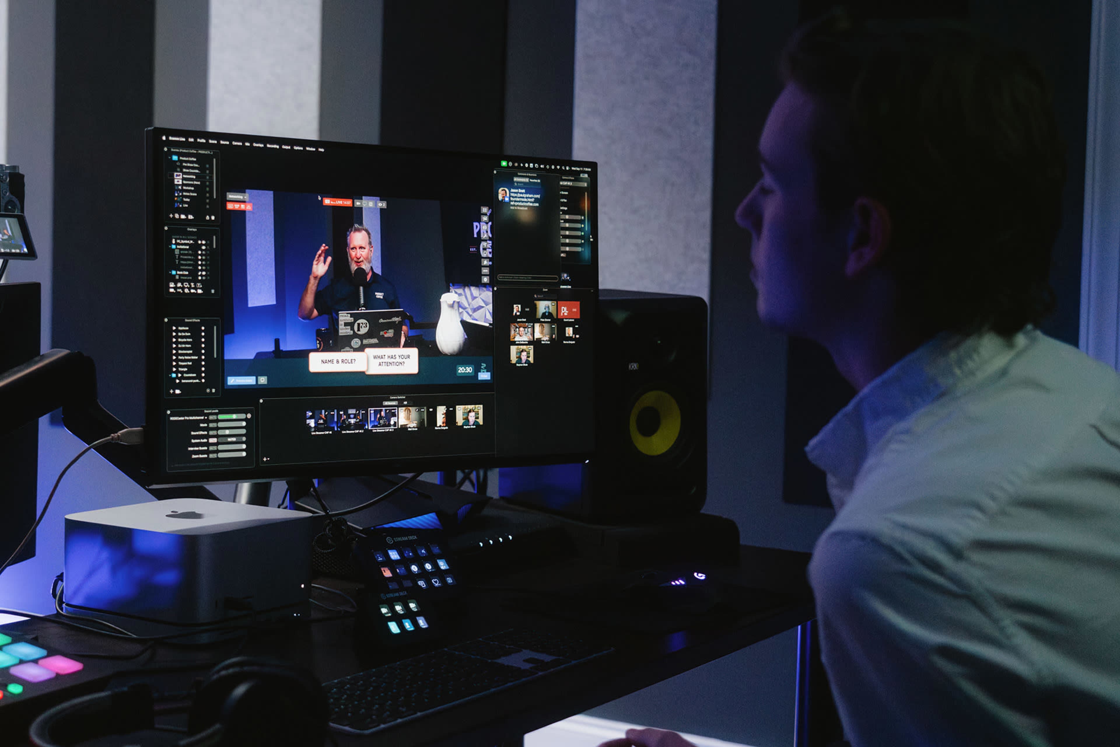 A person sits at a desk, focused on a computer screen displaying a livestream or video call interface with multiple participants.