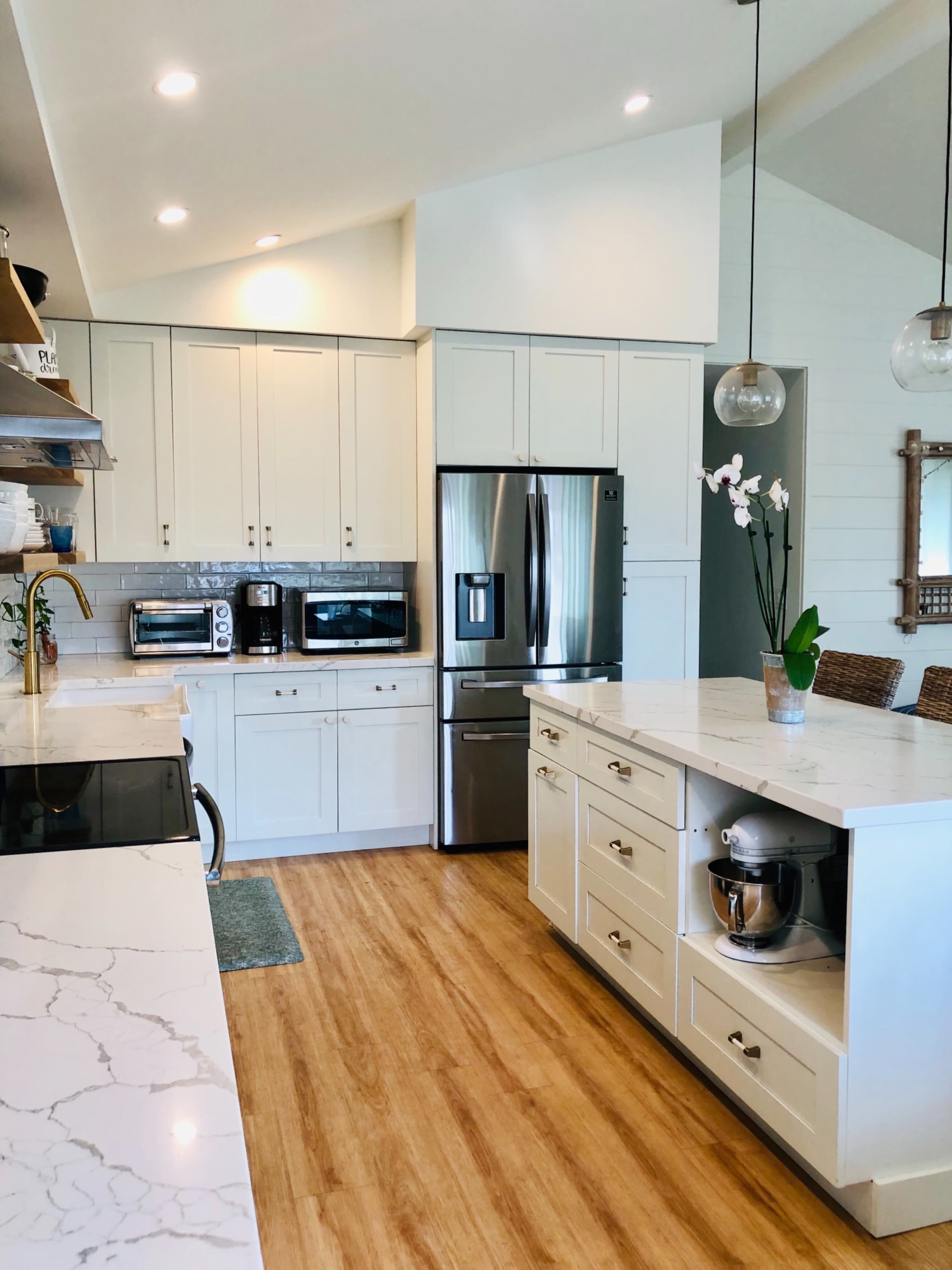 A modern kitchen features white cabinetry, stainless steel appliances, and a large island with a marble countertop.