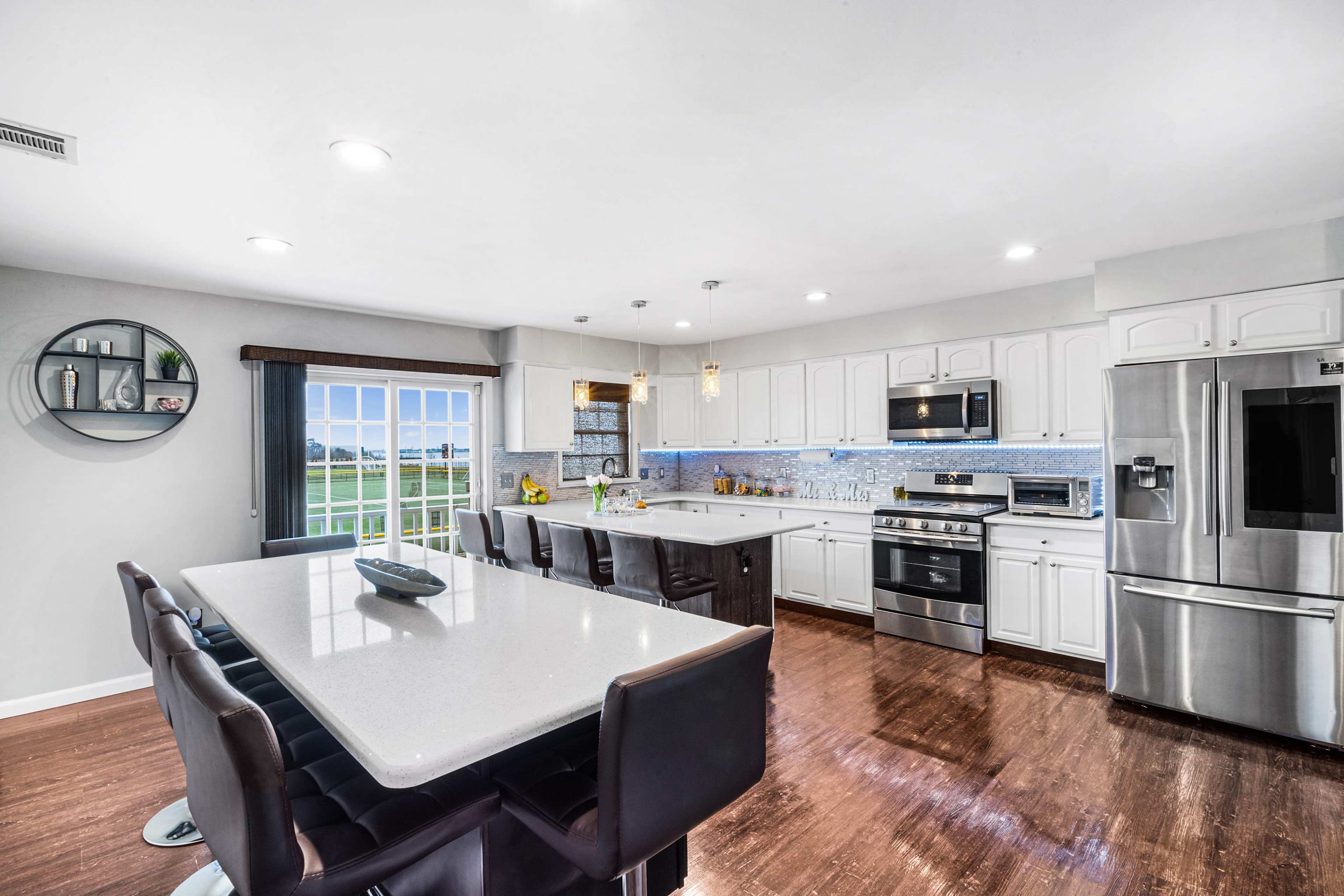 A modern kitchen features a large island with seating, stainless steel appliances, white cabinetry, and a window with a view.