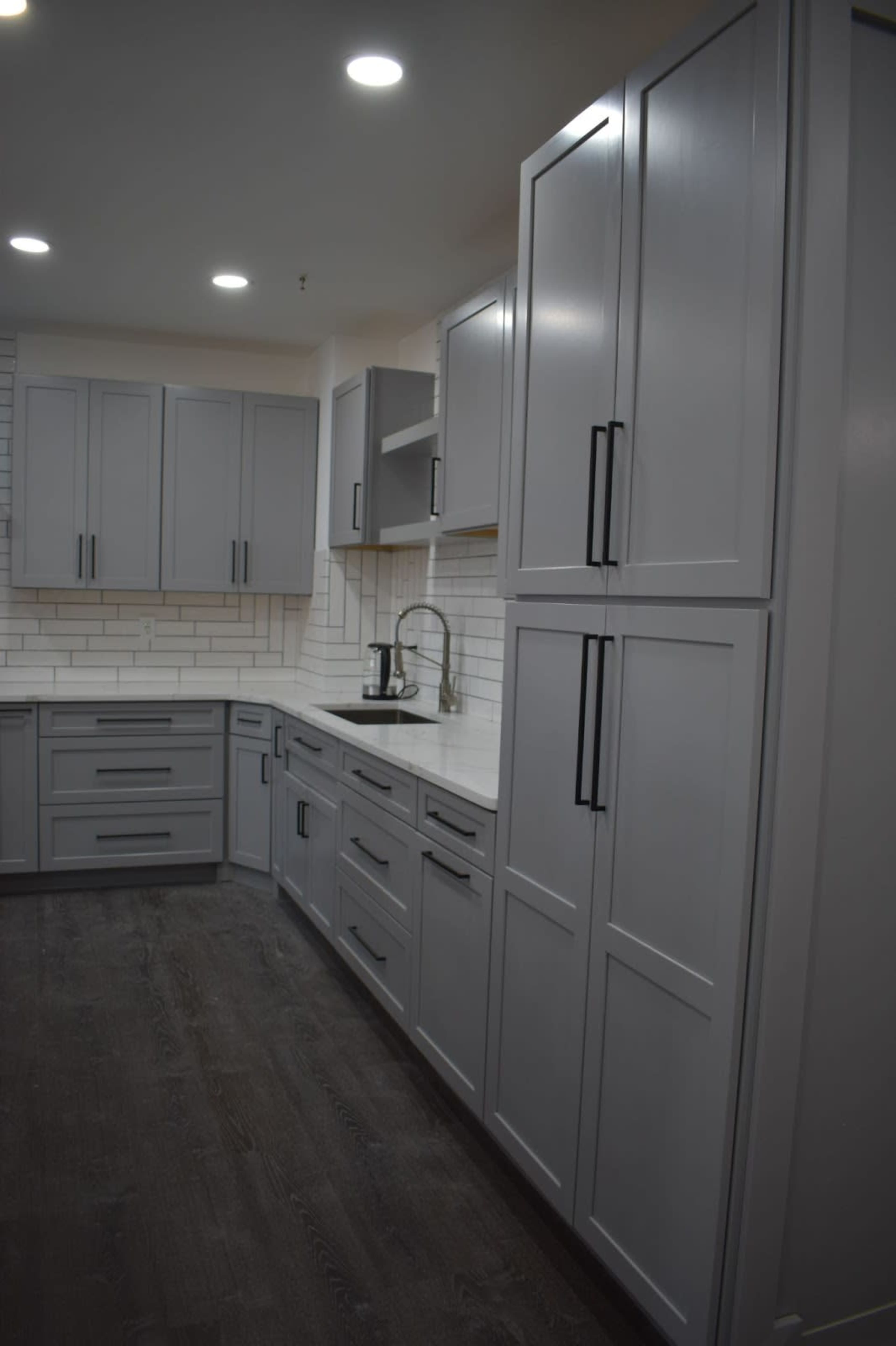 A modern kitchen with gray cabinets, a white countertop, and a tiled backsplash.