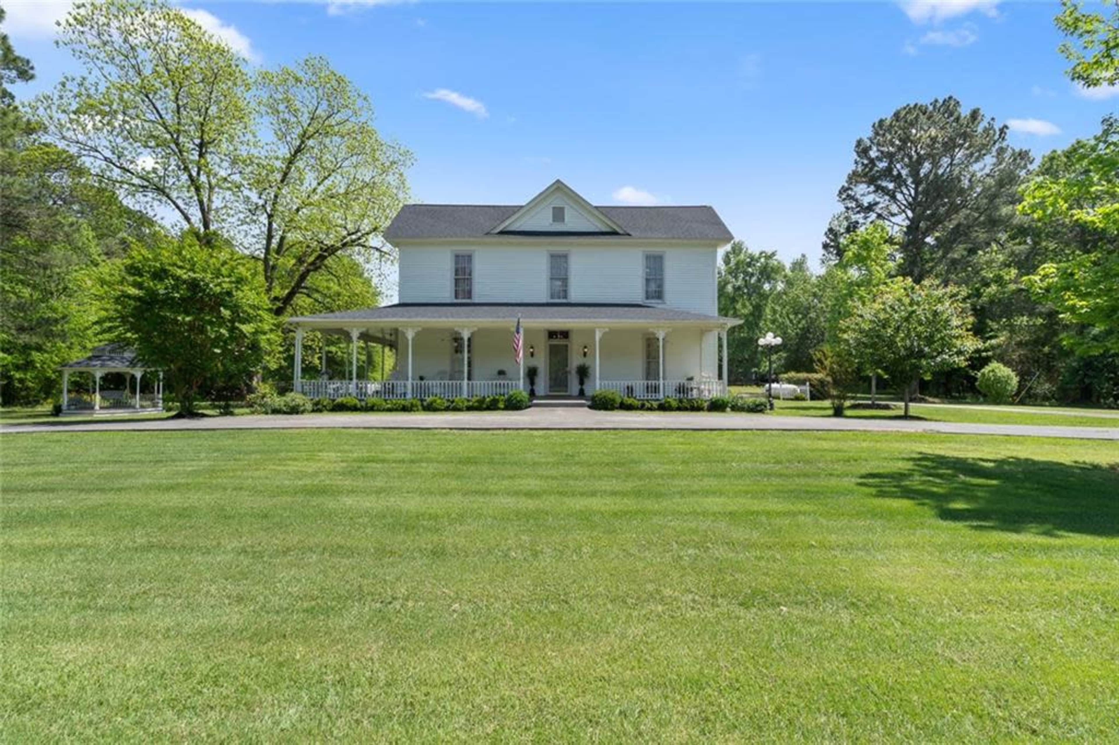 A two-story yellow house with a wide porch is surrounded by a manicured lawn and trees.