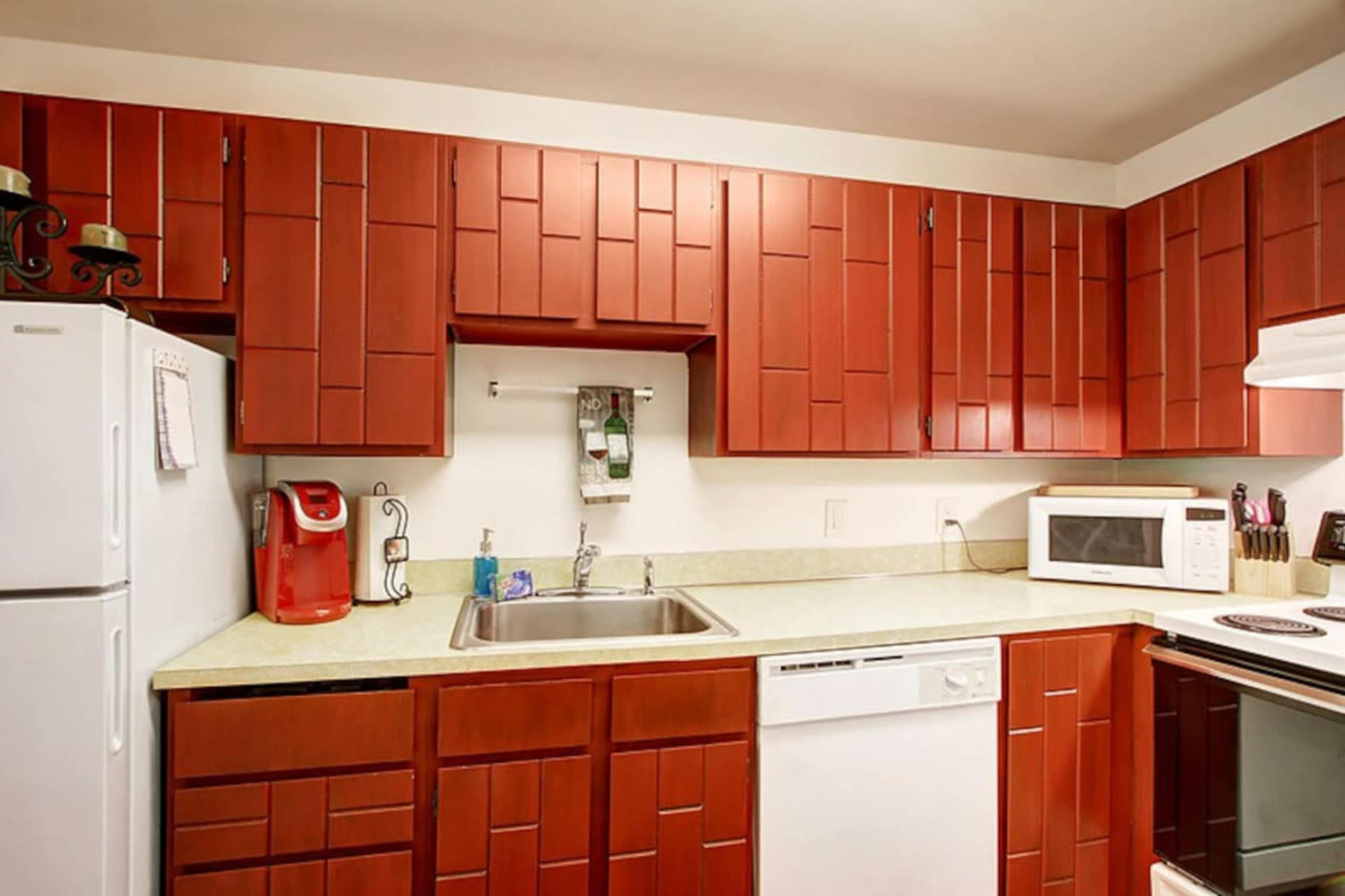 The image shows a kitchen with red cabinetry, a white refrigerator, a sink, a dishwasher, a microwave, and a stove.