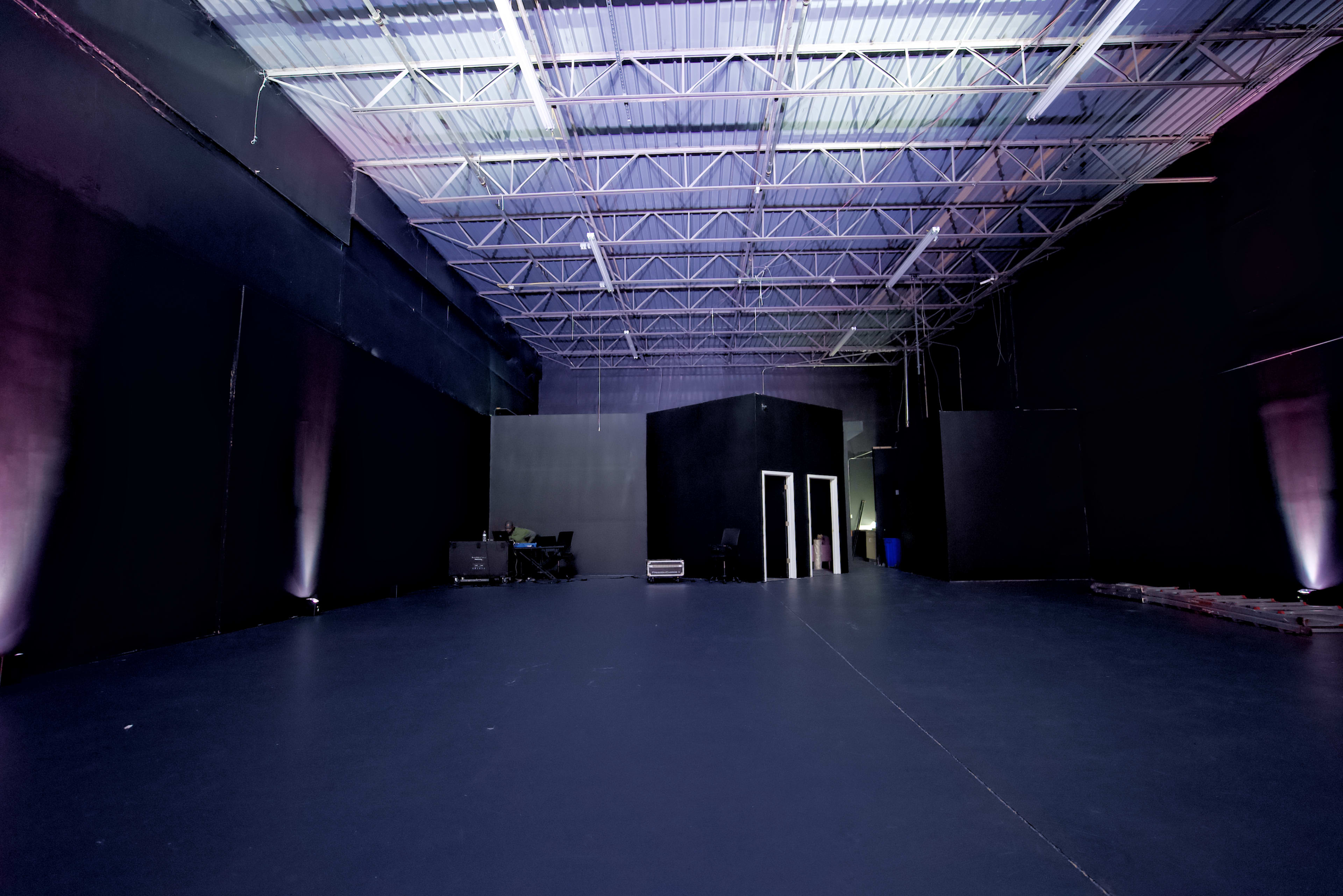 The image shows a large, empty studio space with black walls and a smooth, dark floor under artificial lighting.