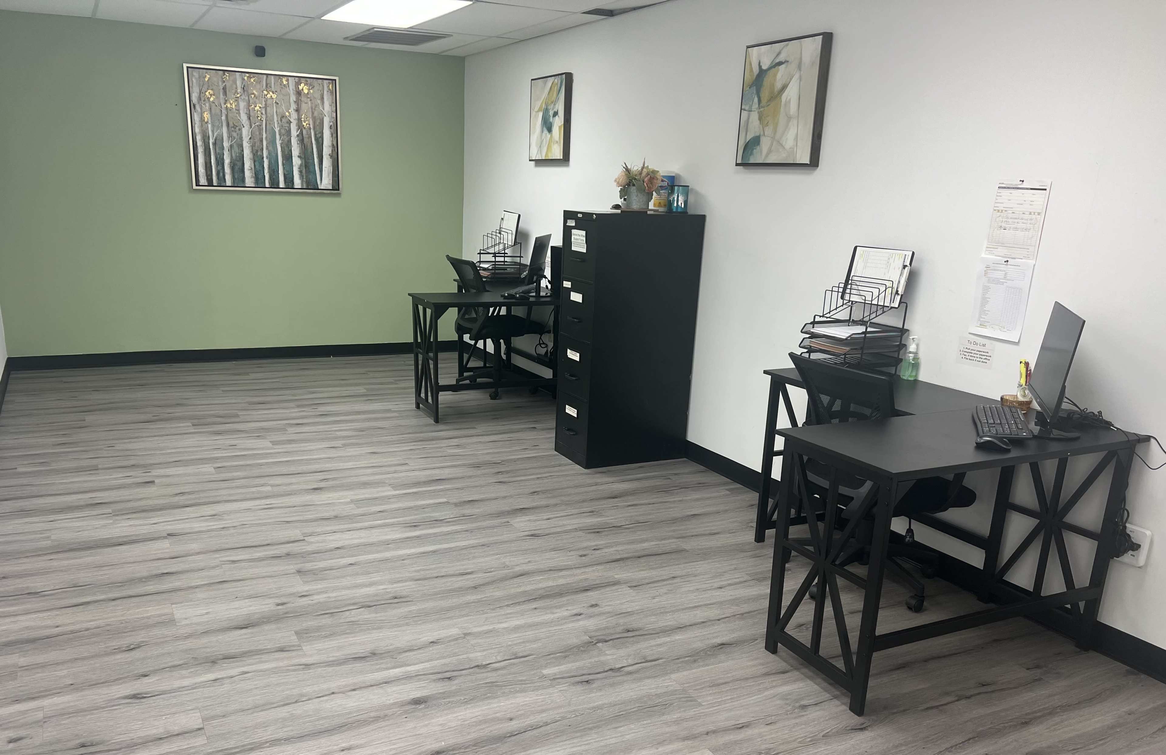 An empty office space with two desks, a filing cabinet, and green accent walls.