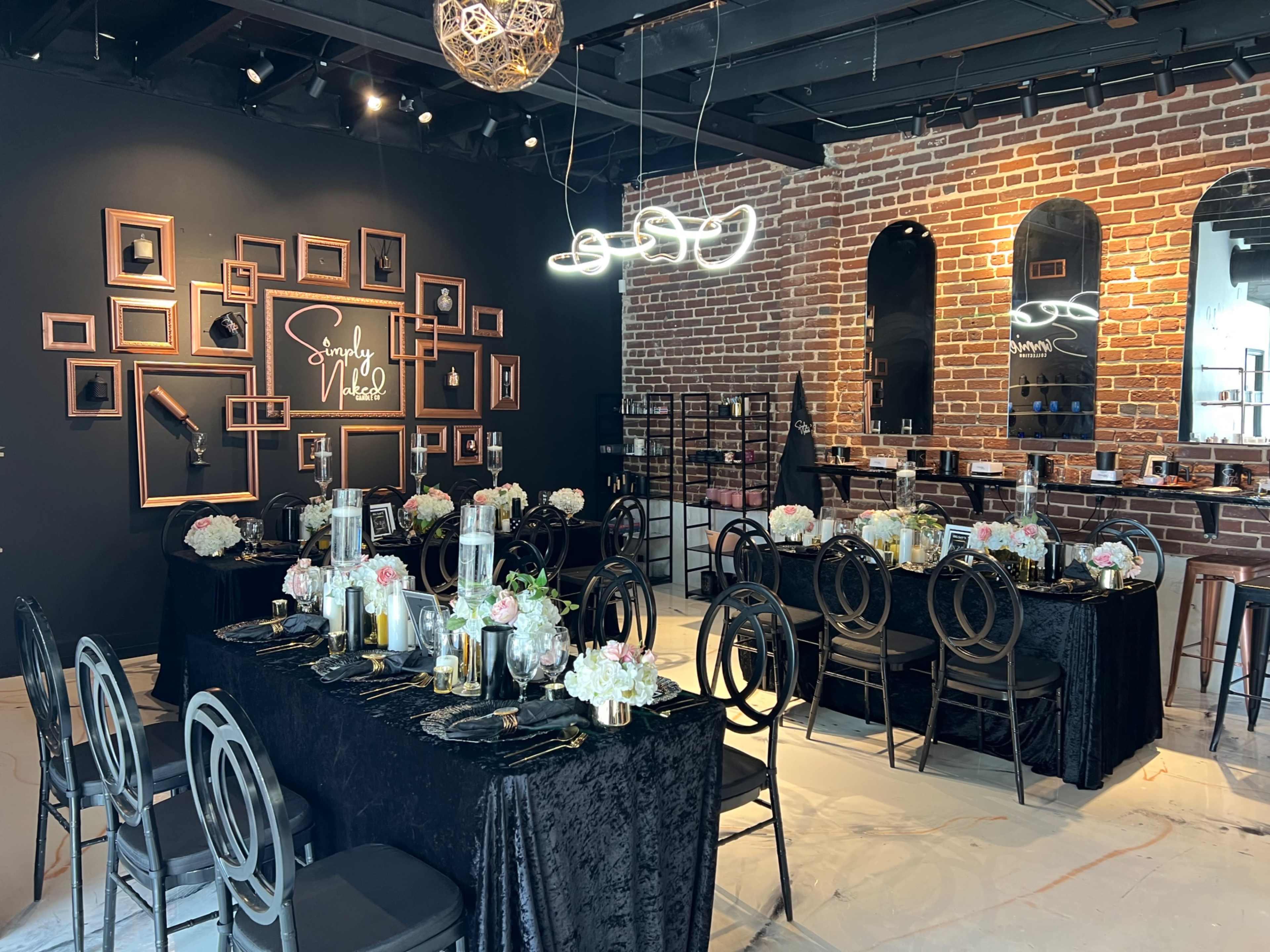 A stylish event space with black tables adorned with floral centerpieces, framed photos on the wall, and modern lighting fixtures.
